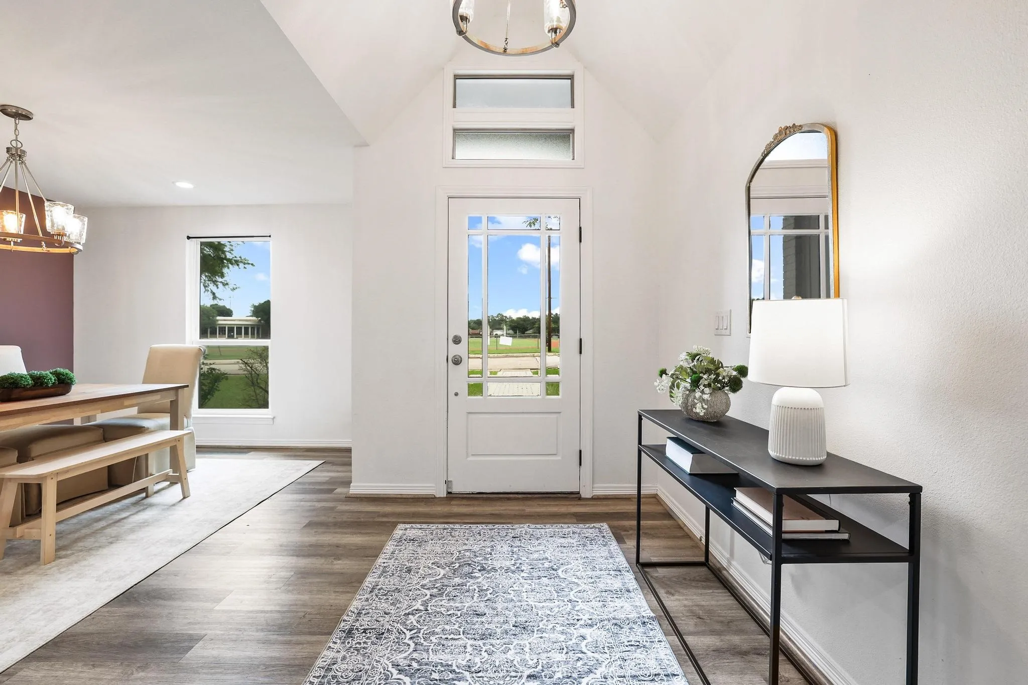Vaulted entryway with wood-finish flooring, transom windows, and a glass-paneled entry door