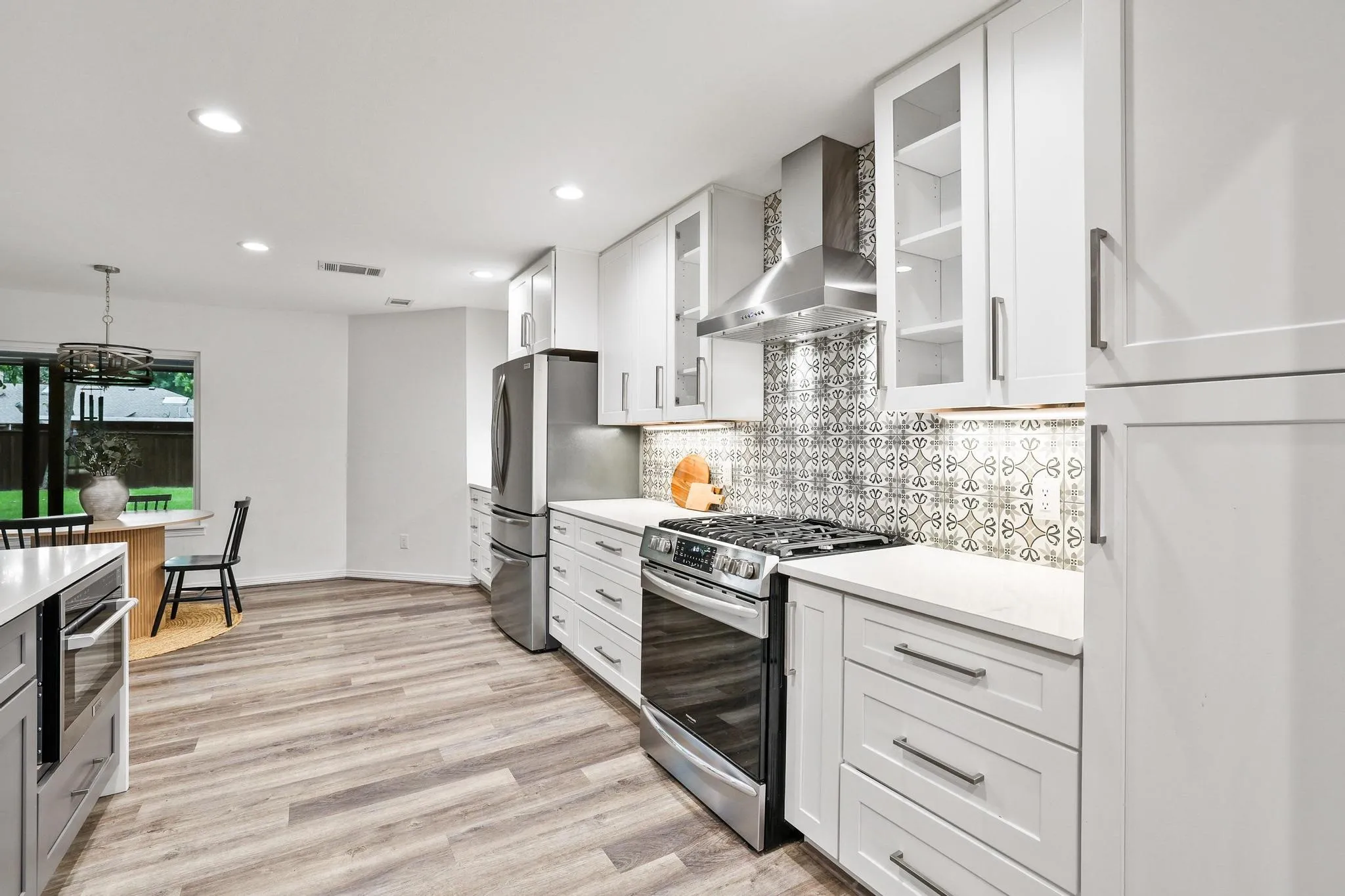 Modern kitchen featuring white shaker cabinetry, patterned tile backsplash, stainless steel appliances, and wood-finish flooring
