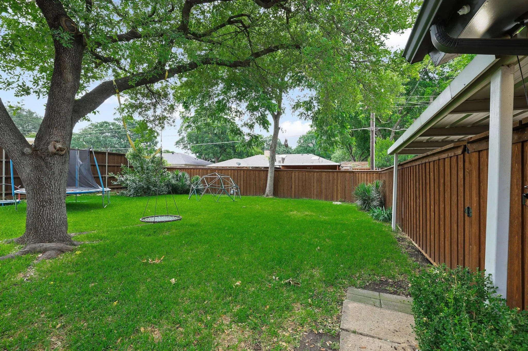 Expansive backyard featuring a mature tree, concrete stepping stones, and a full privacy fence