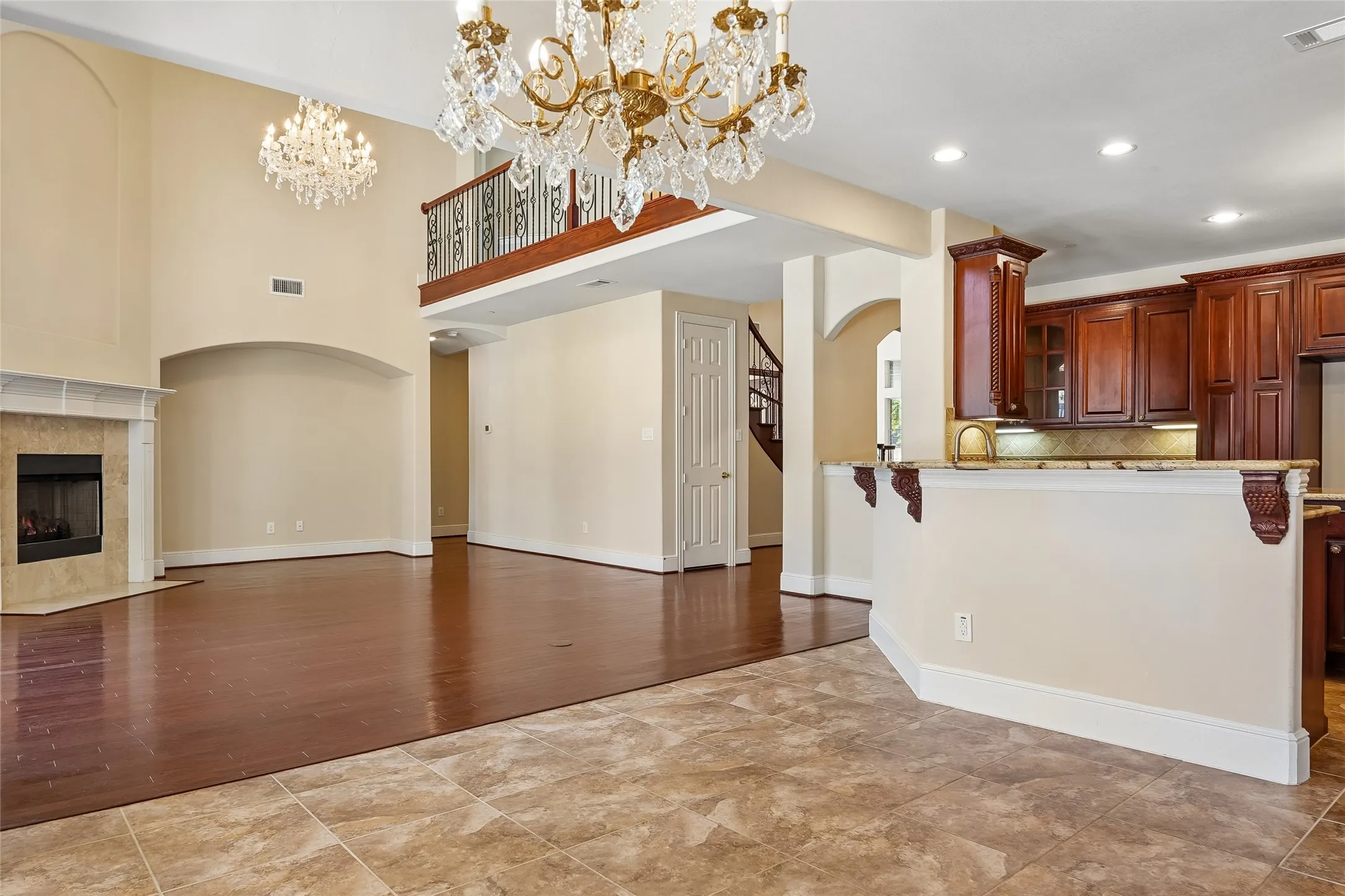Two-story living area with a fireplace, wood-finish flooring, and two crystal chandeliers