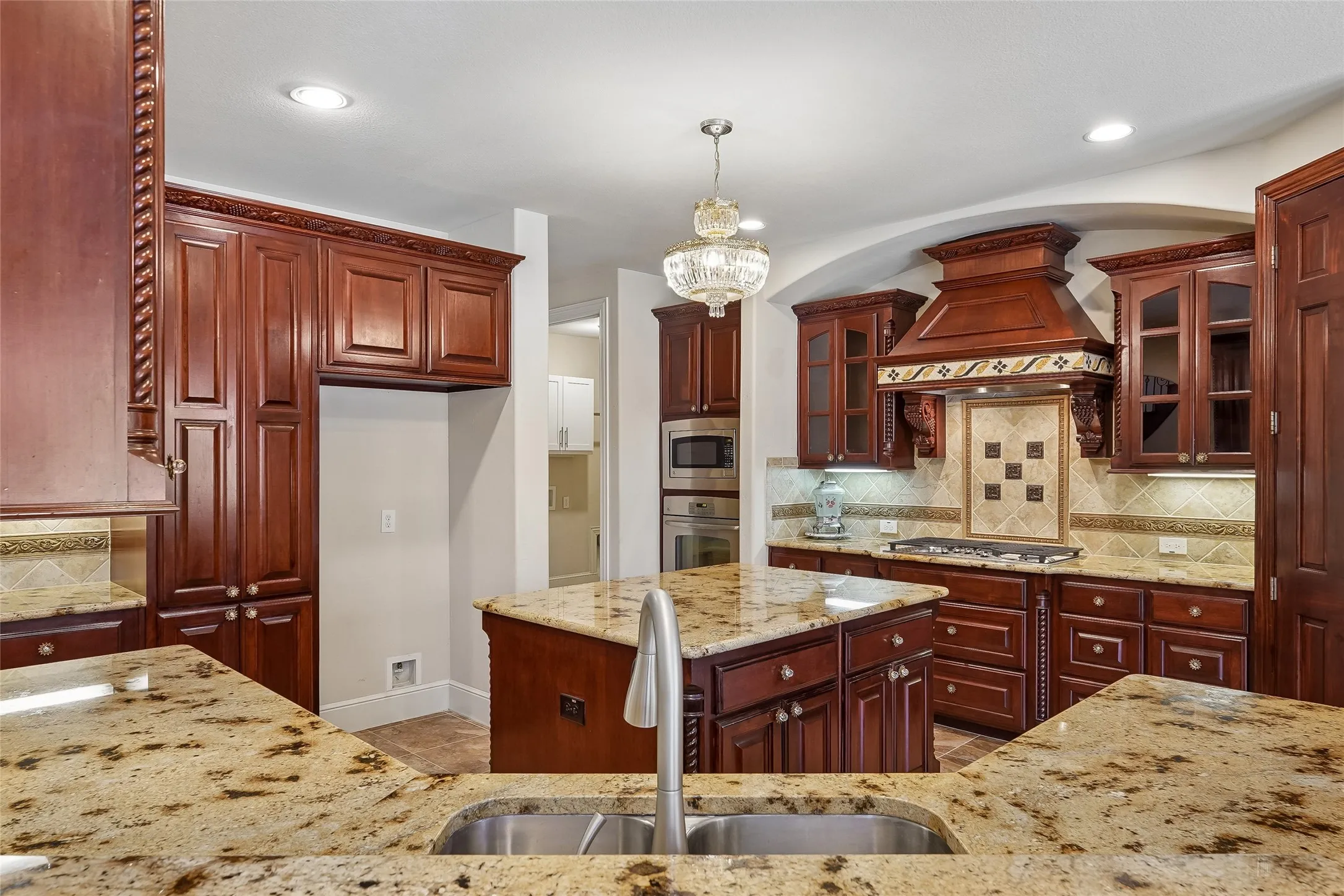 Spacious kitchen featuring rich wood cabinetry, granite countertops, a central island, stainless steel sink with a gooseneck faucet, and integrated stainless steel appliances