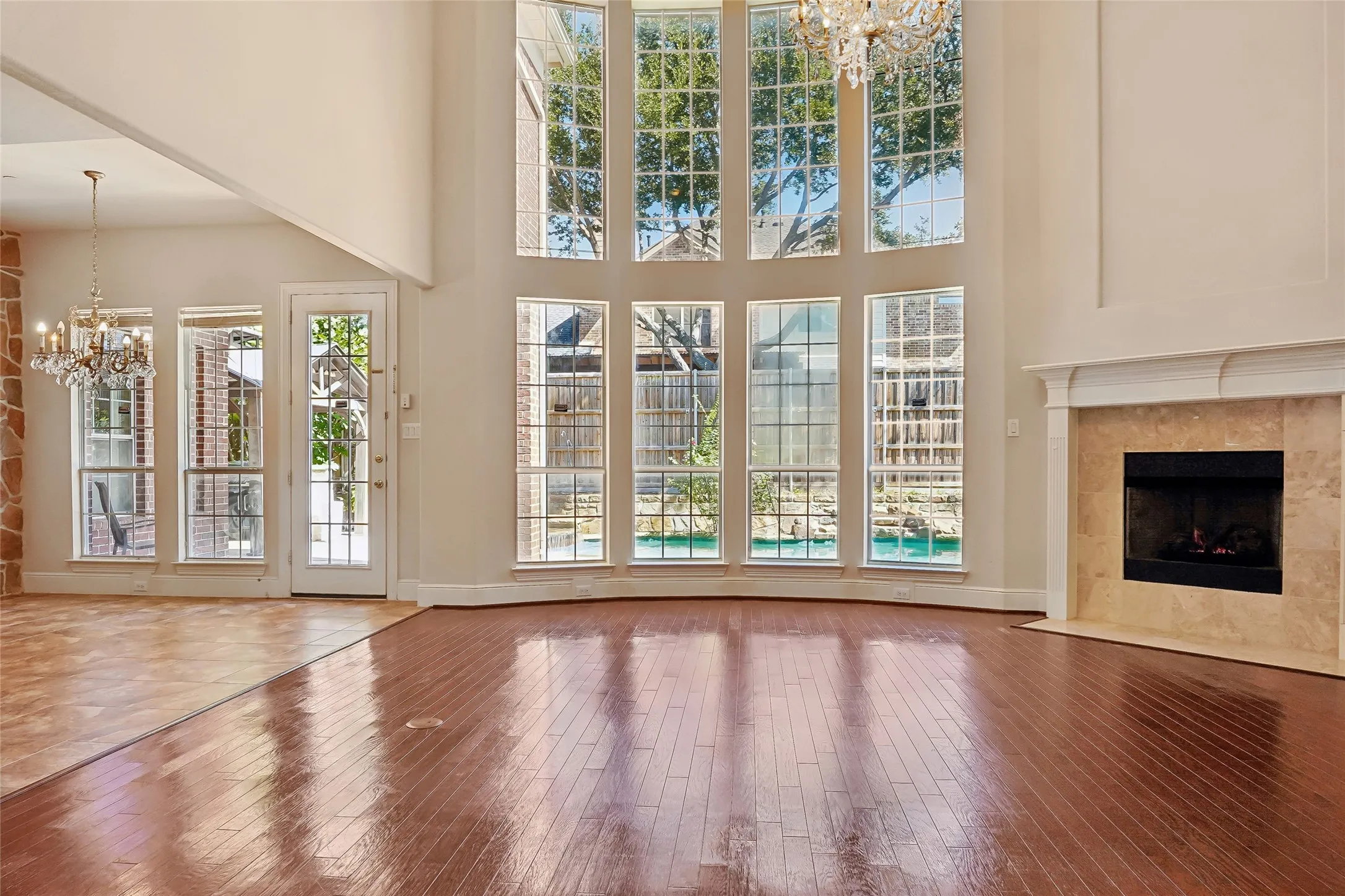 Two-story living area with wood-finish flooring, a stone-clad fireplace with a white mantel, and large picture windows