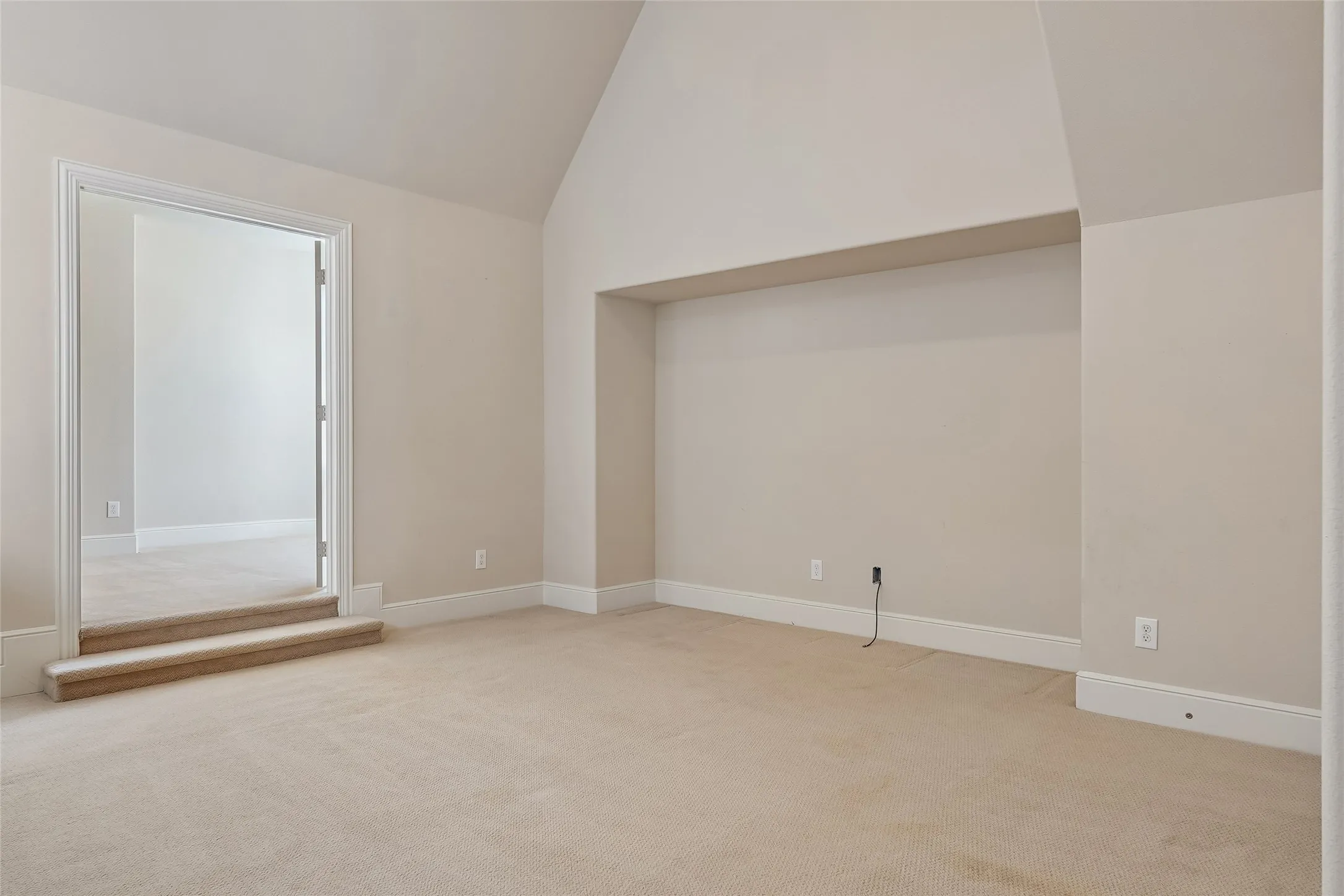 Vaulted ceiling, neutral tone carpeting, recessed wall niche, and crisp white trim