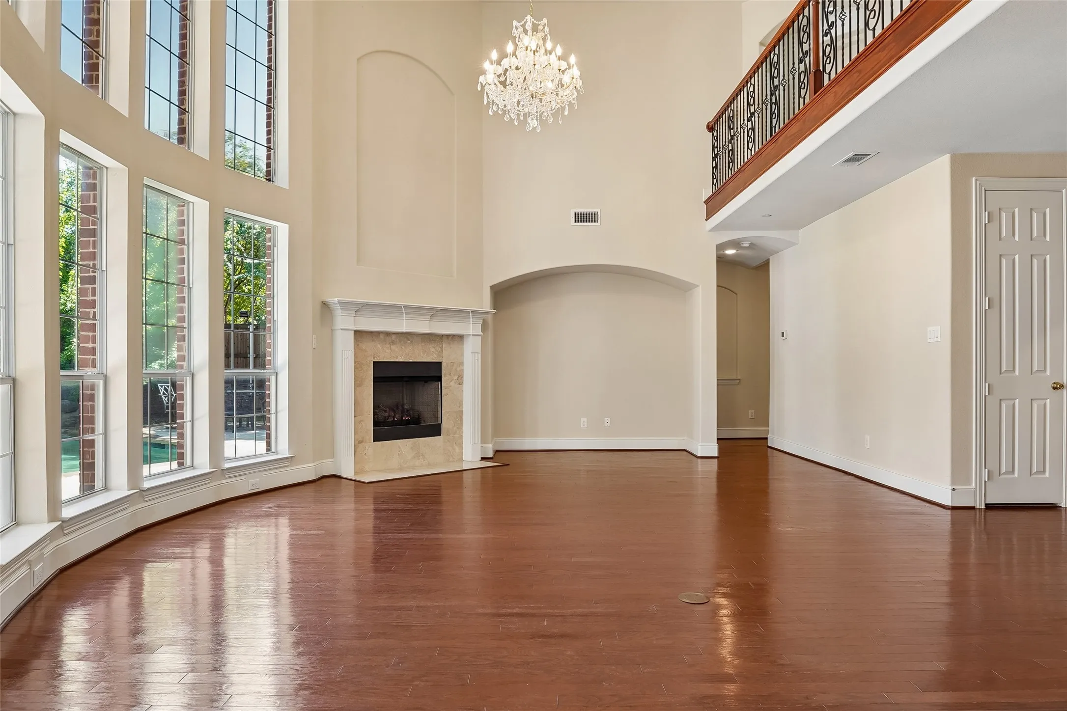 Hardwood flooring, high ceilings, decorative chandelier, fireplace with stone surround, and a second-story balcony with an iron railing