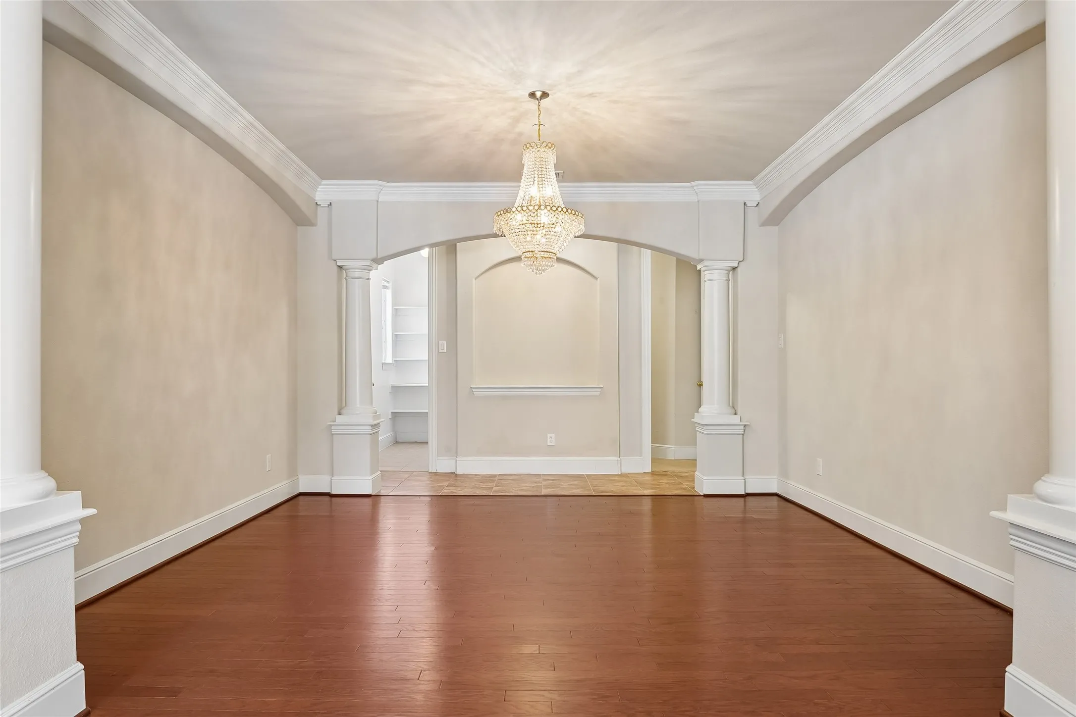 Hardwood flooring, decorative chandelier, arched entryway, architectural columns, and crown molding