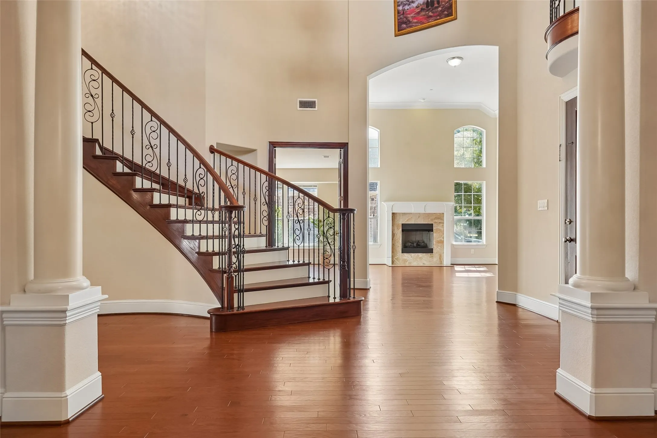 Hardwood flooring throughout, grand staircase with wrought iron balusters, high ceilings, arched doorways, and a fireplace with a stone surround