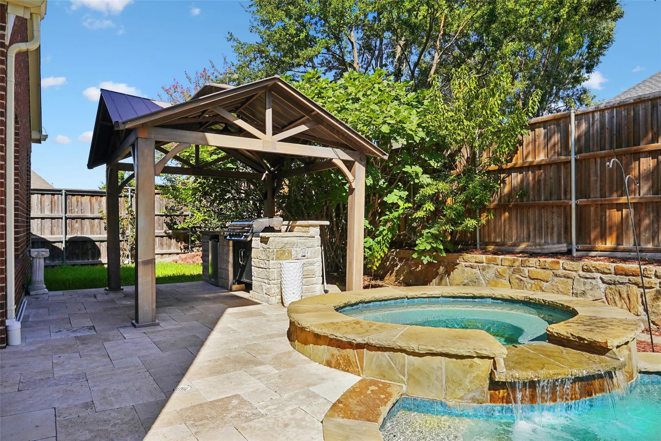 Stone paver patio featuring a covered outdoor kitchen, built-in grill, and a spa with a waterfall feature