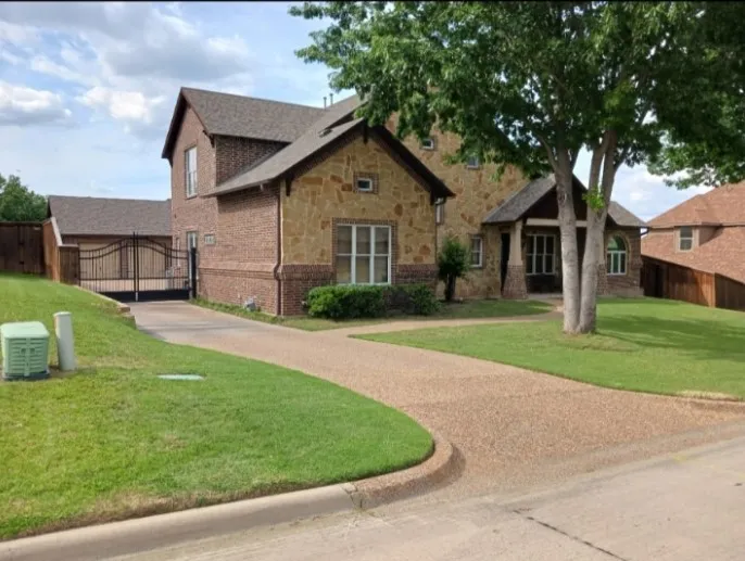Curved driveway behind a wrought iron gate, with a mature shade tree and brick and stone front