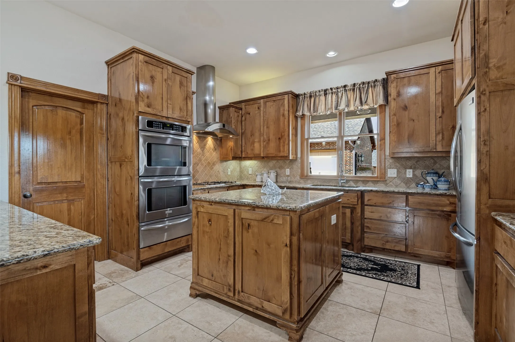 Kitchen with knotty alder cabinets, granite island, stainless double ovens, and a vent hood