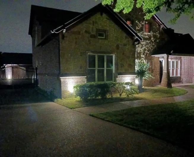 Lit side elevation, with the walkway and the gated driveway beyond