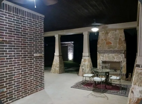 Covered patio with a stained wood ceiling, stone columns, and an outdoor fireplace