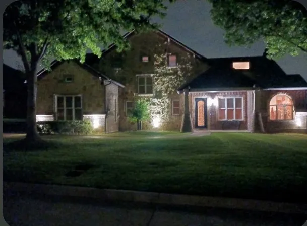 Front of the home at dusk, with landscape uplighting on the brick and stone