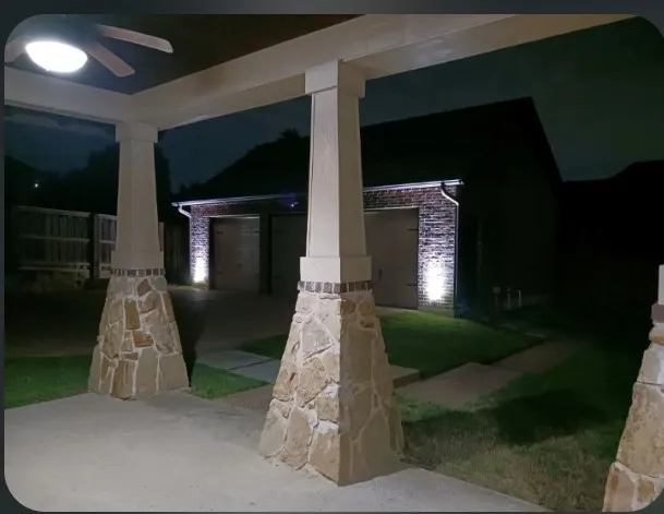 Covered patio at night with stone columns, looking out to the lit detached 3-car garage