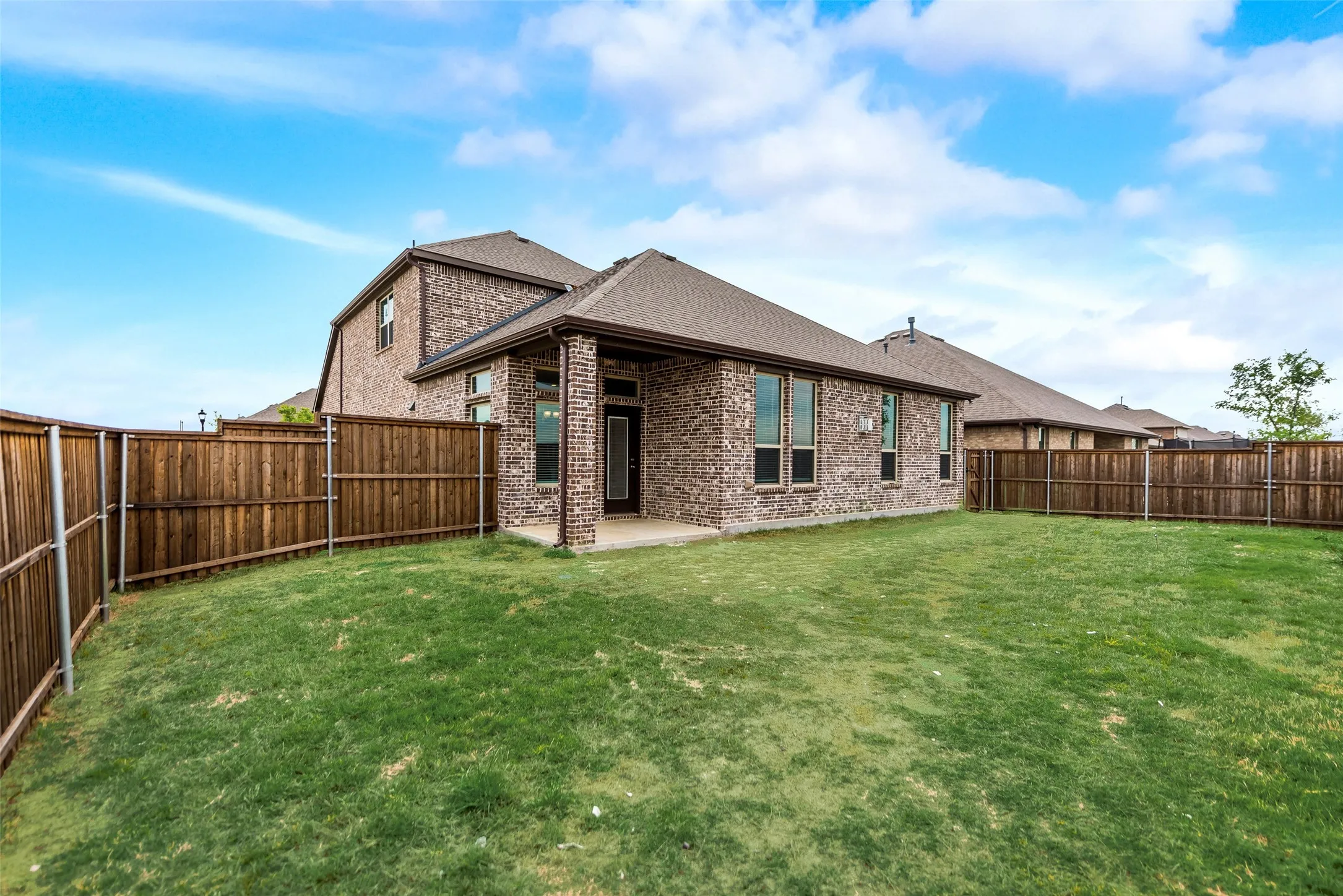 Brick exterior with multiple windows, covered patio, and a privacy fence enclosing a grassy yard