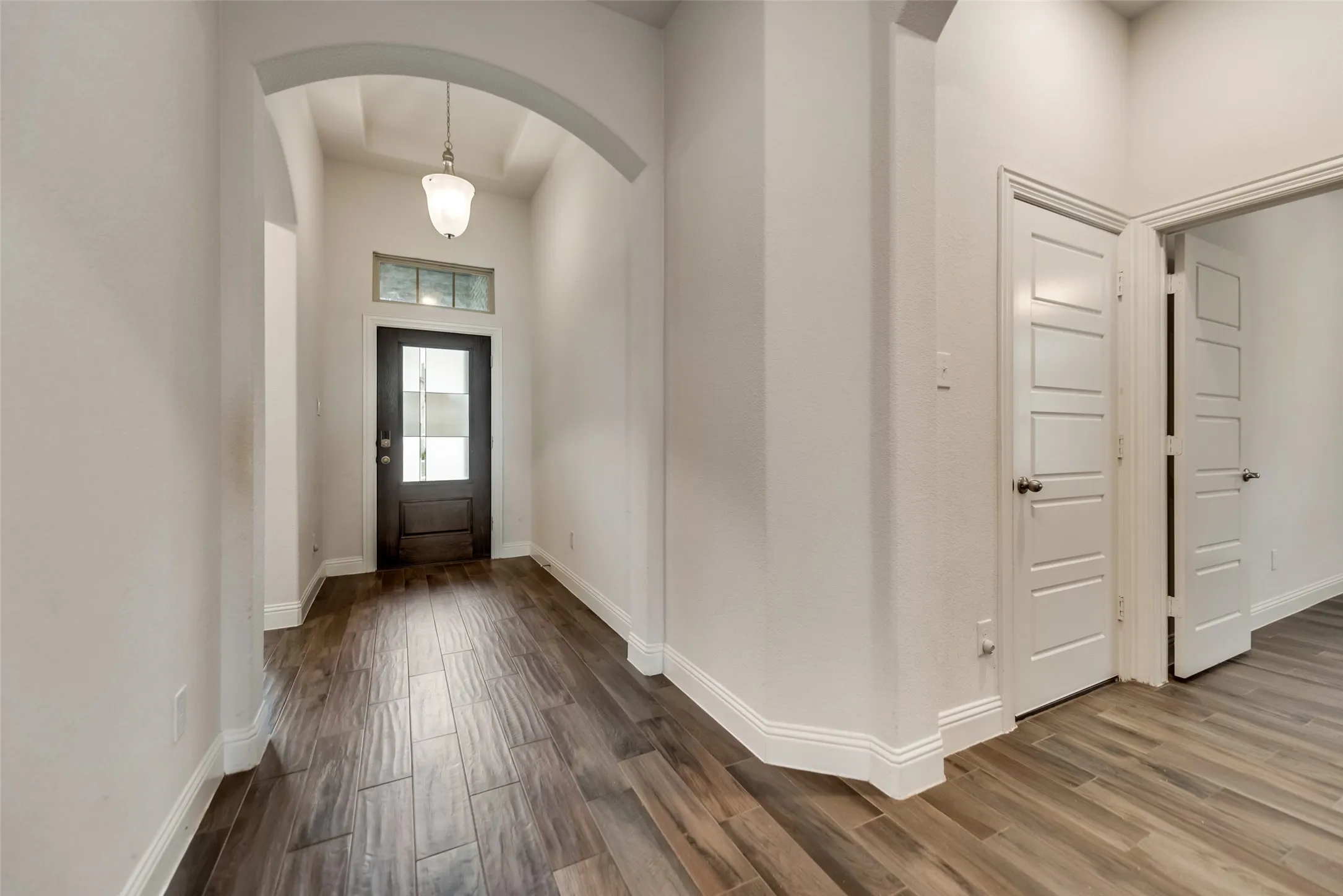 Arched entryway with a dark wood-paneled door, transom window, and wood-finish tile flooring