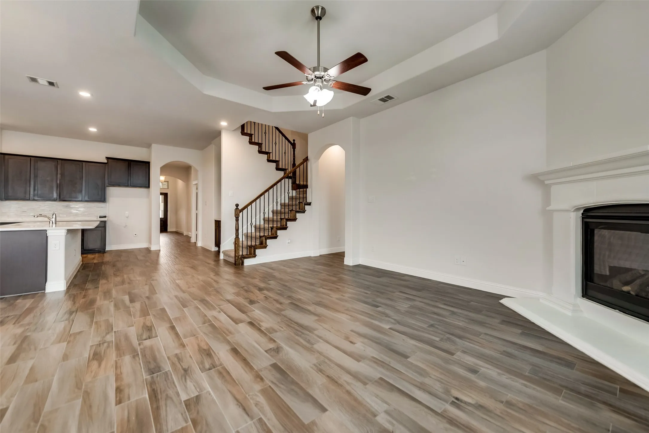 Spacious living area featuring wood-finish flooring, a decorative fireplace, a tray ceiling, and a built-in ceiling fan
