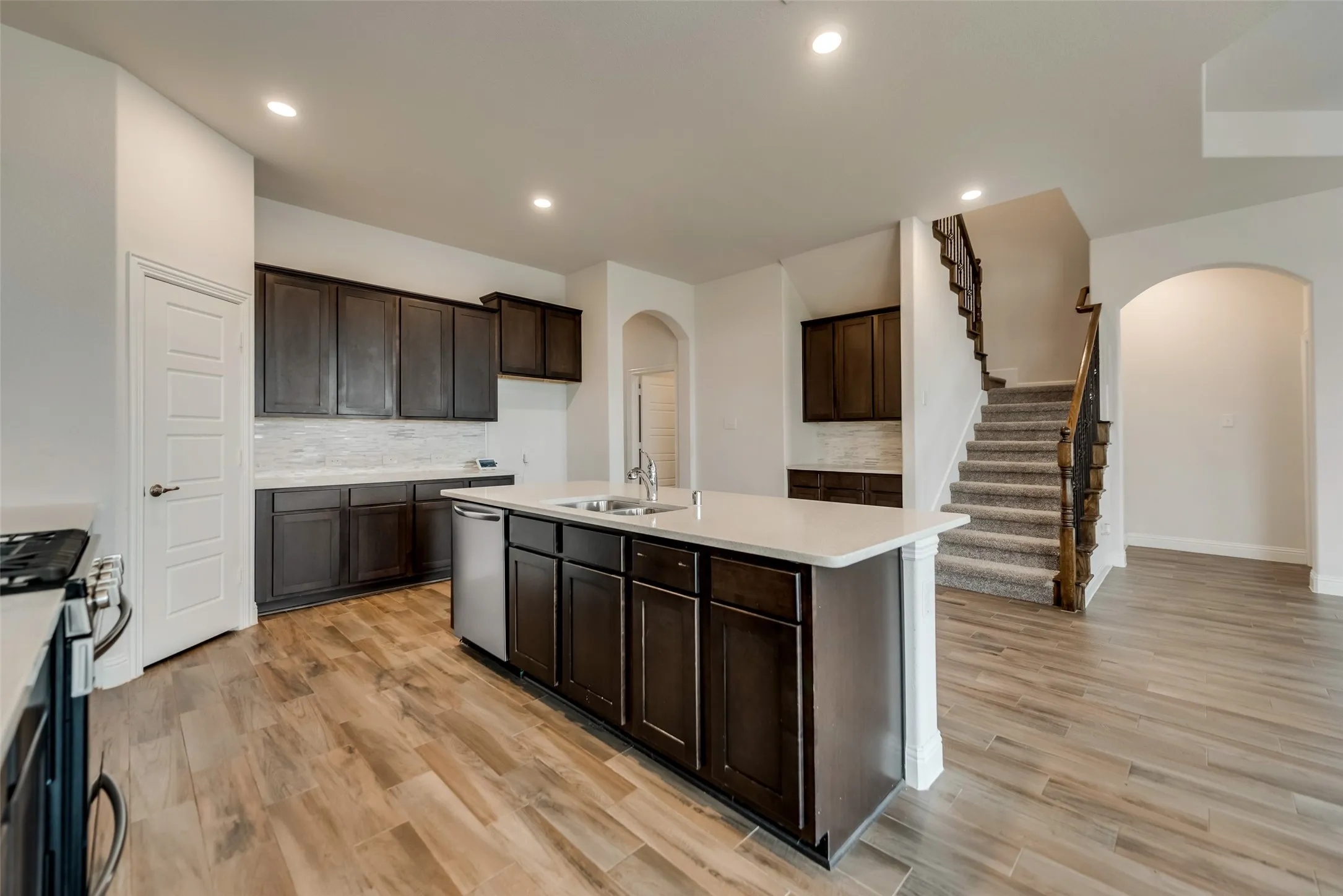 Kitchen featuring wood-finish flooring, dark wood cabinetry, a center island with countertop seating, stainless steel appliances, and recessed lighting