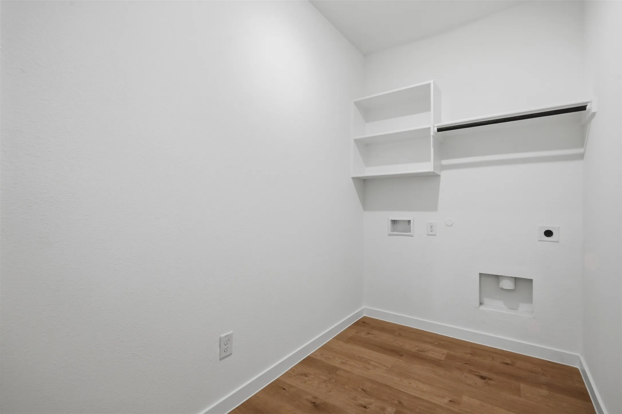 Laundry area featuring wood-finish flooring, white walls, and built-in shelving with a hanging rod