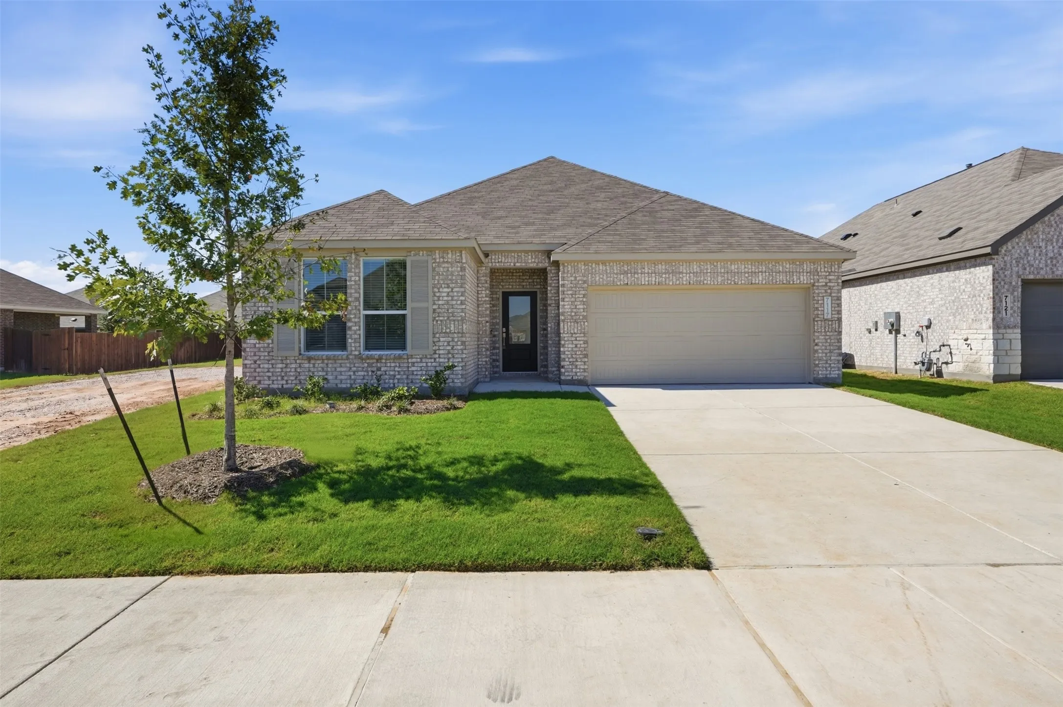 Light-colored brick exterior with gray shutters, a two-car garage, concrete driveway, and a well-maintained lawn
