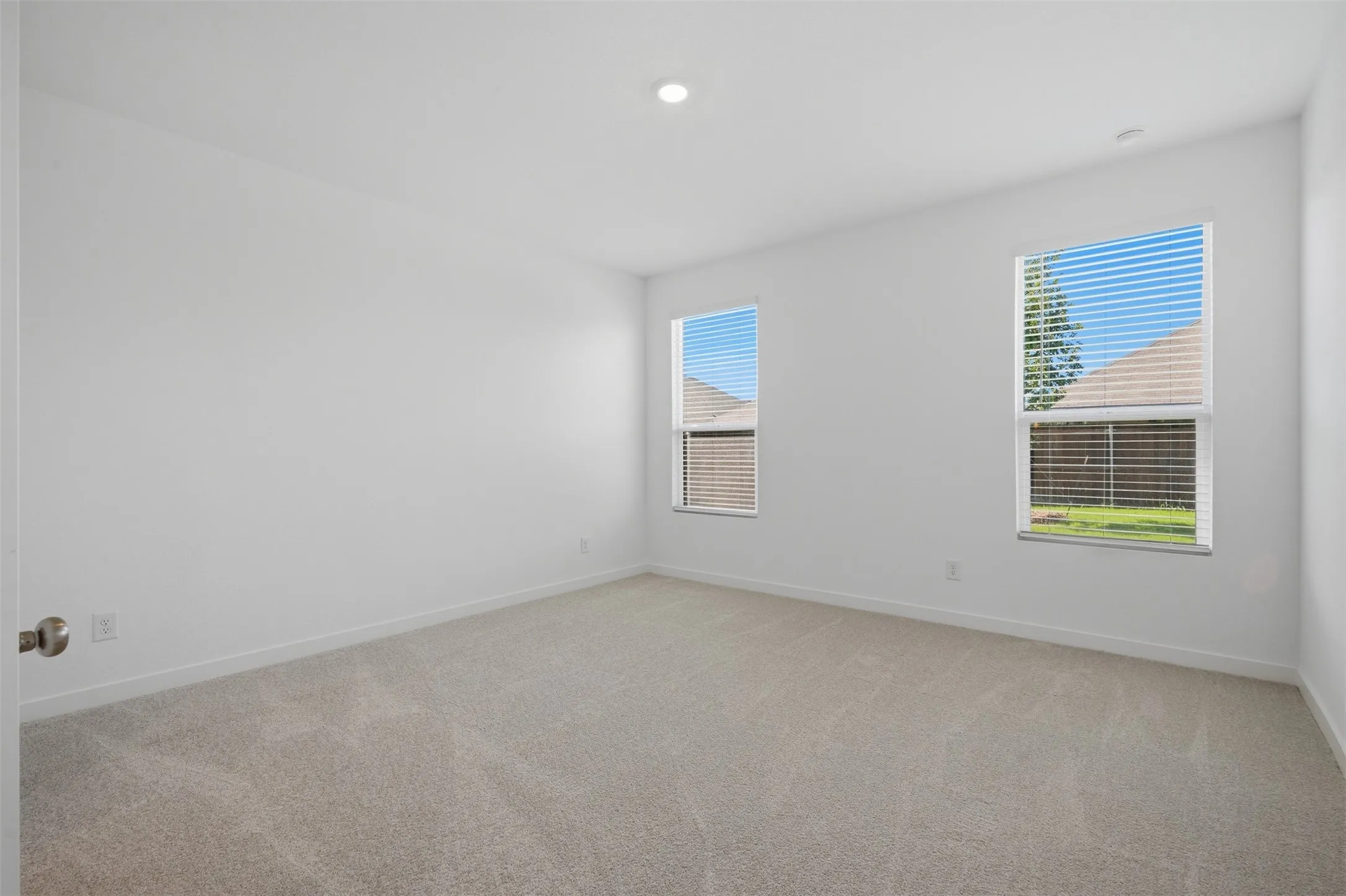 Recessed lighting, neutral wall paint, two windows with blinds, and light-toned carpeting