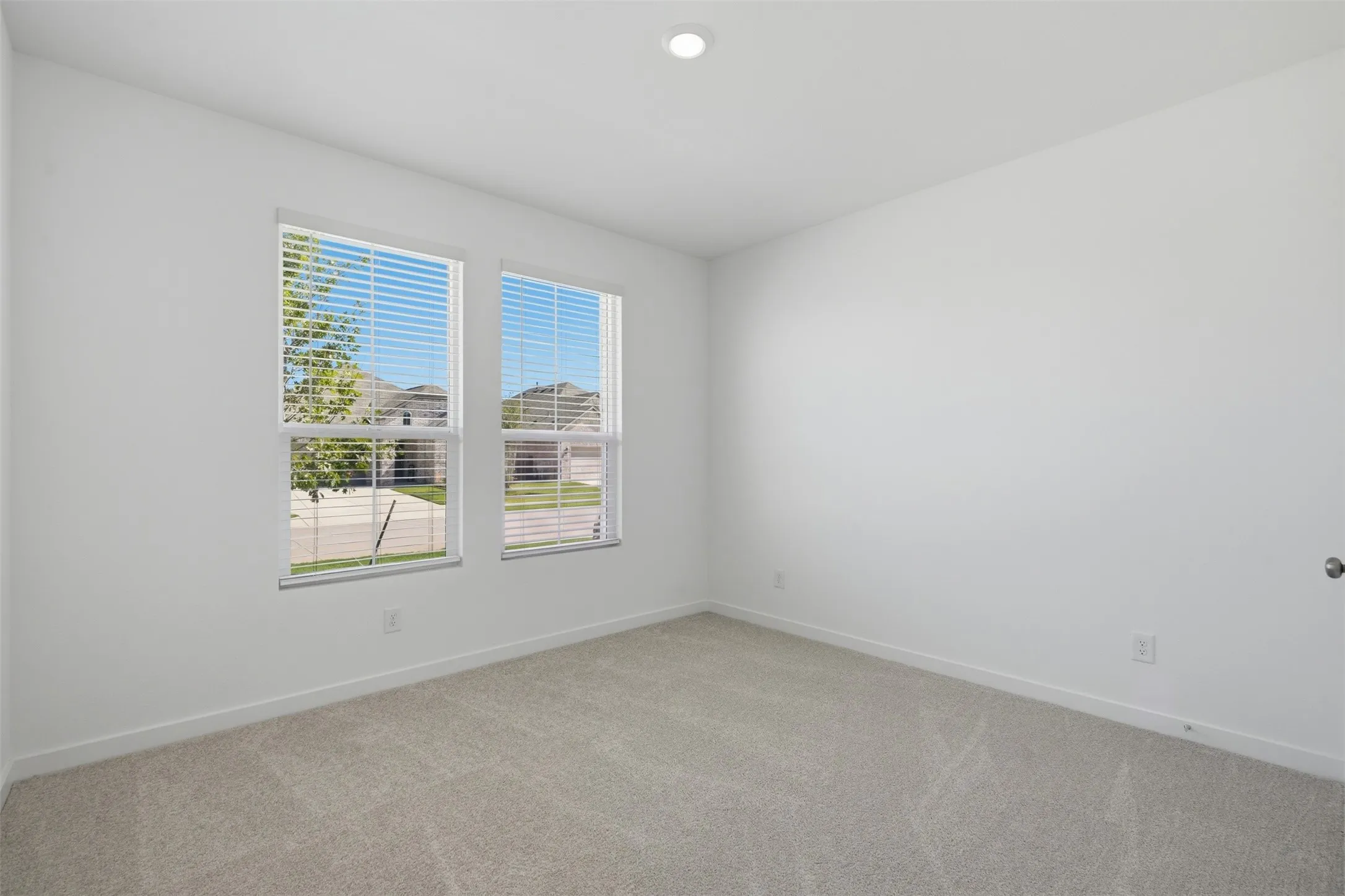 Neutral wall color, recessed lighting, double windows with blinds, and light-toned carpet flooring