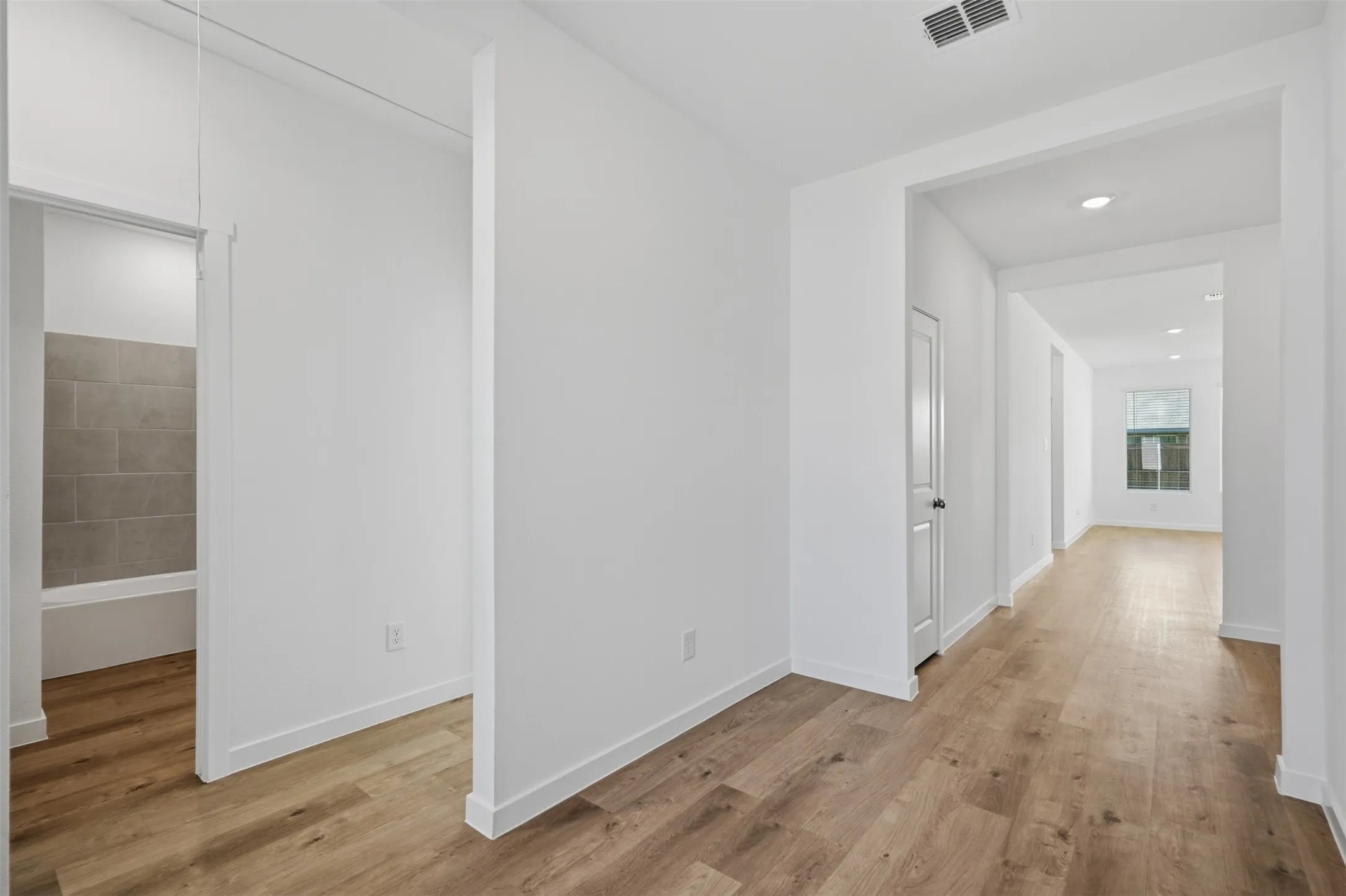 White painted interior with wood-finish flooring, recessed lighting, and a neutral tile bathtub surround