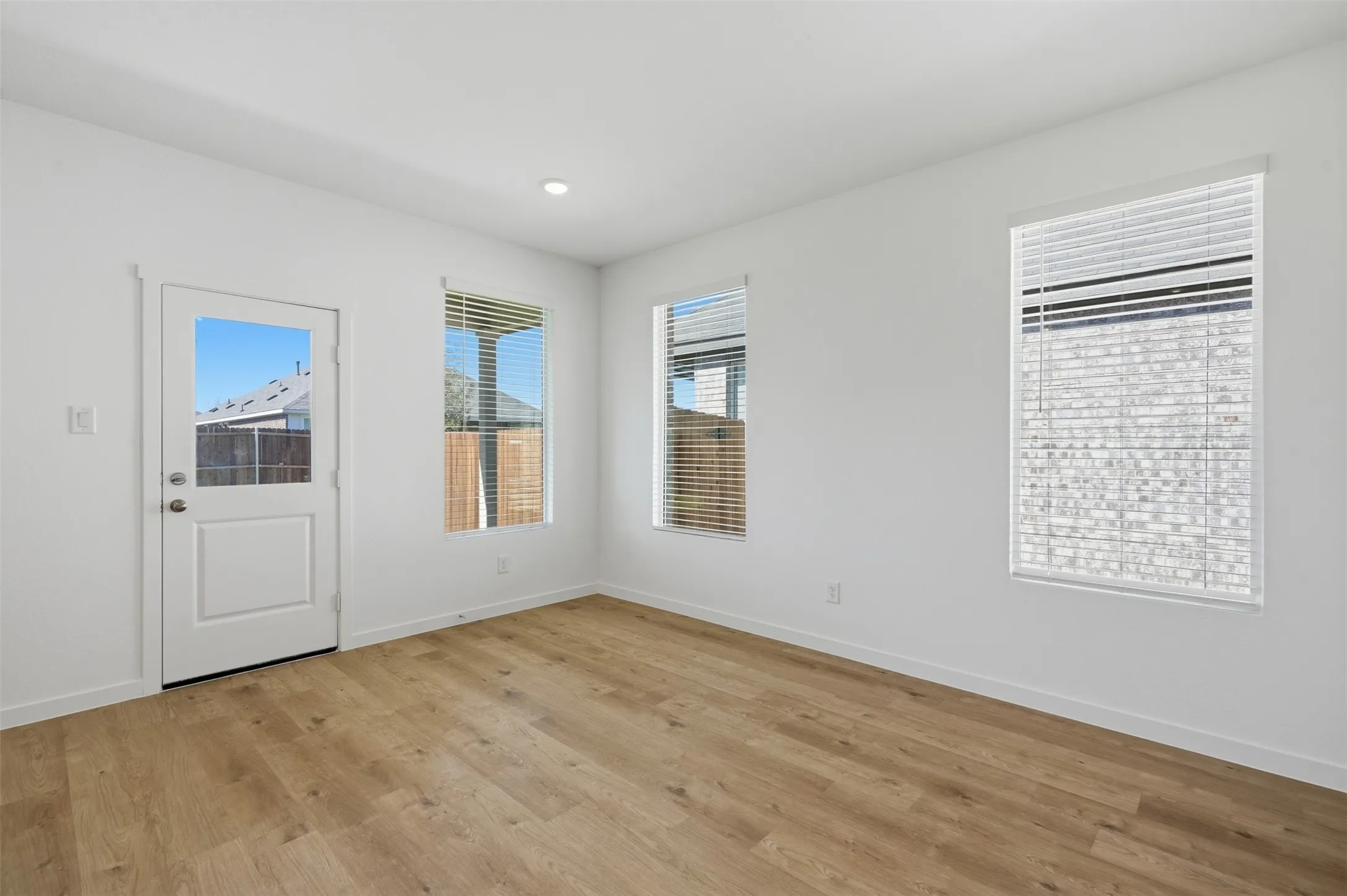 Room featuring wood-finish flooring, recessed lighting, and multiple windows with blinds