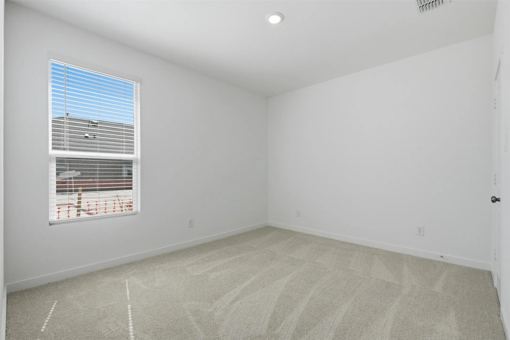 Carpeted flooring, single window with horizontal blinds, recessed ceiling light, white painted walls