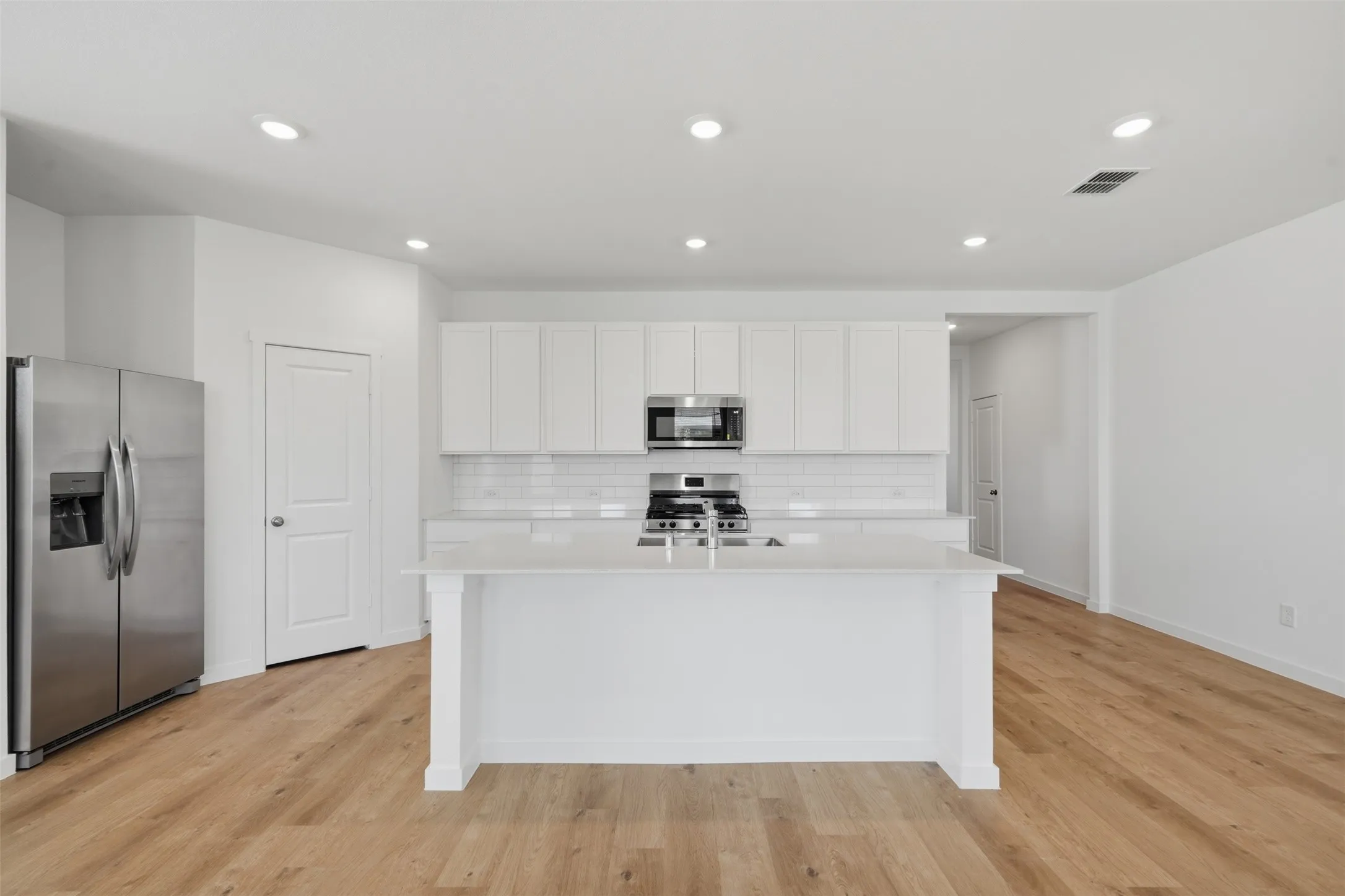 Kitchen featuring a central island, stainless steel appliances, recessed lighting, white cabinetry, and wood-finish flooring
