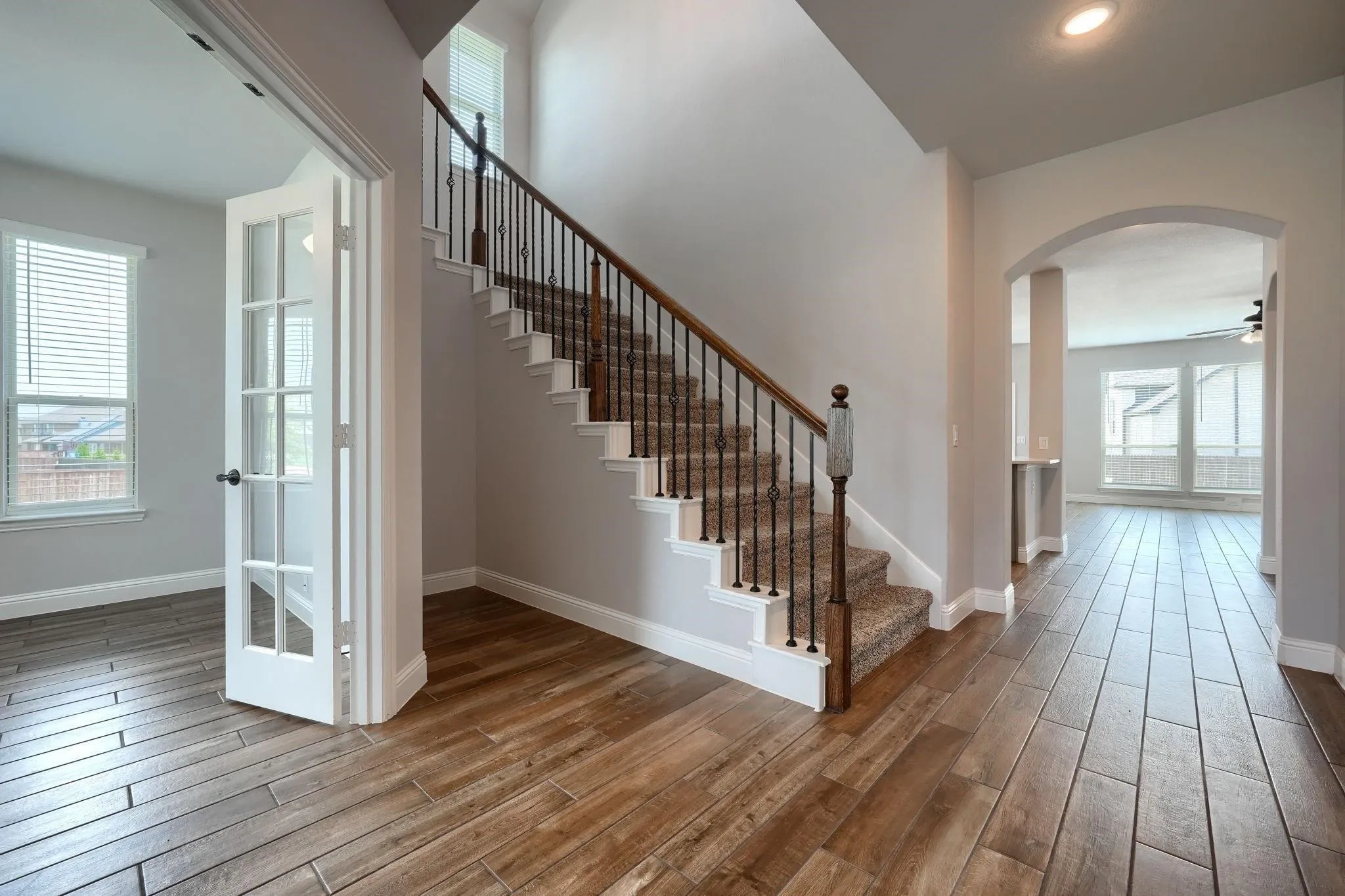 Wood-look tile flooring throughout, staircase with carpeted treads and wrought iron balusters, French doors, arched doorway, and recessed lighting