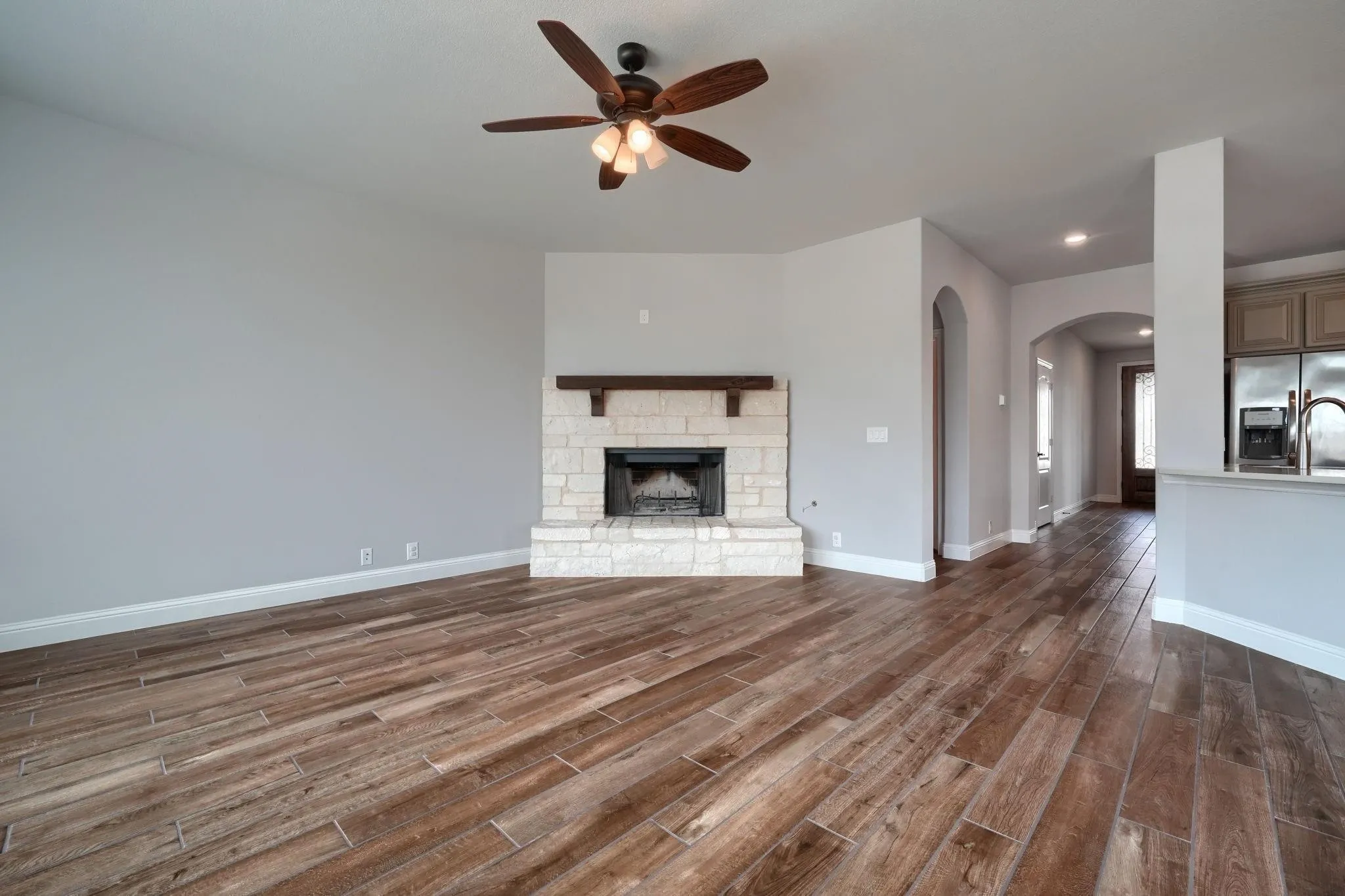 Wood-finish flooring, stone fireplace with wood mantel, vaulted ceiling with ceiling fan, and arched doorways