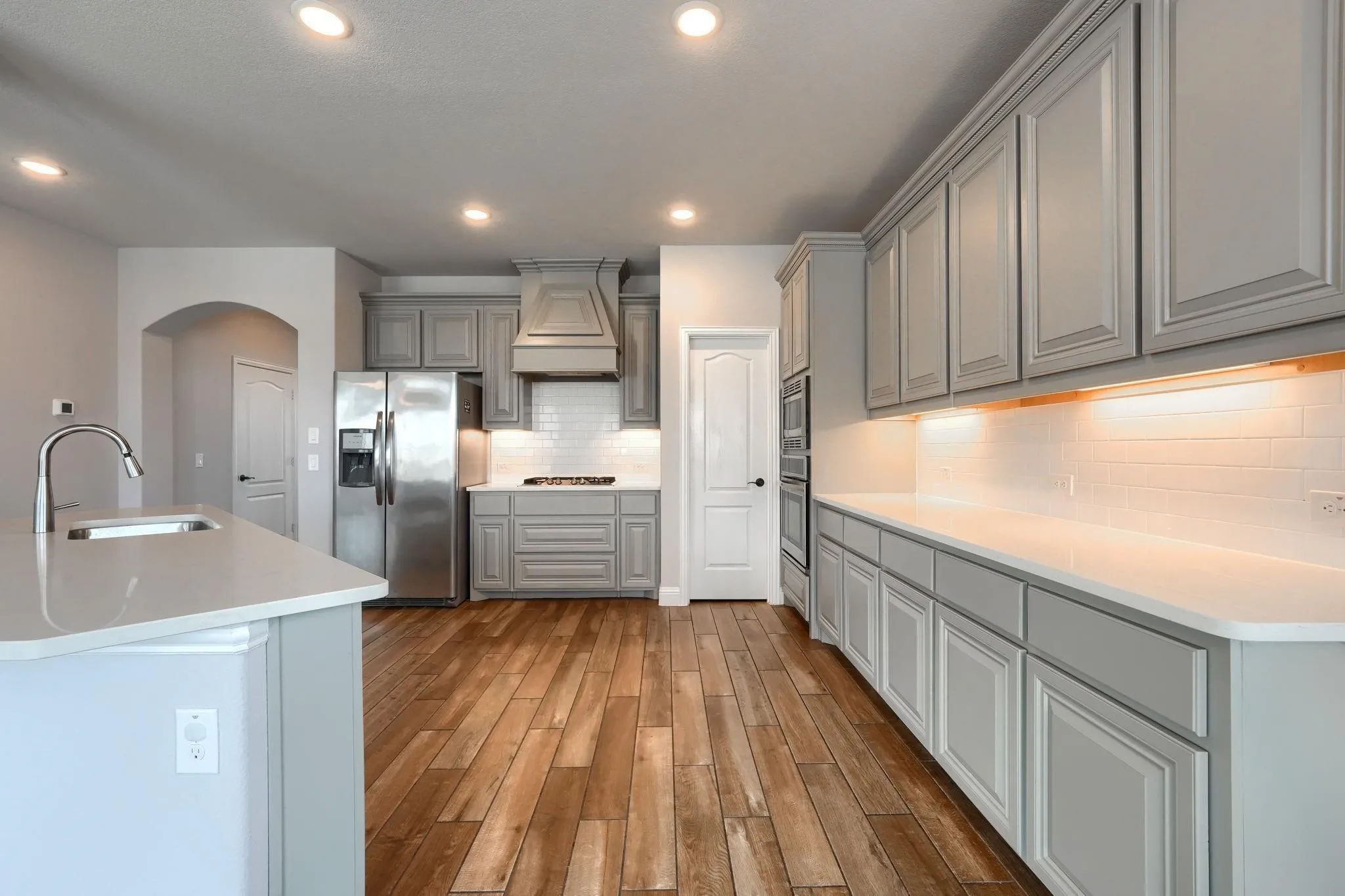Spacious kitchen featuring gray cabinetry, stainless steel appliances, a white subway tile backsplash, recessed lighting, and wood-finish flooring