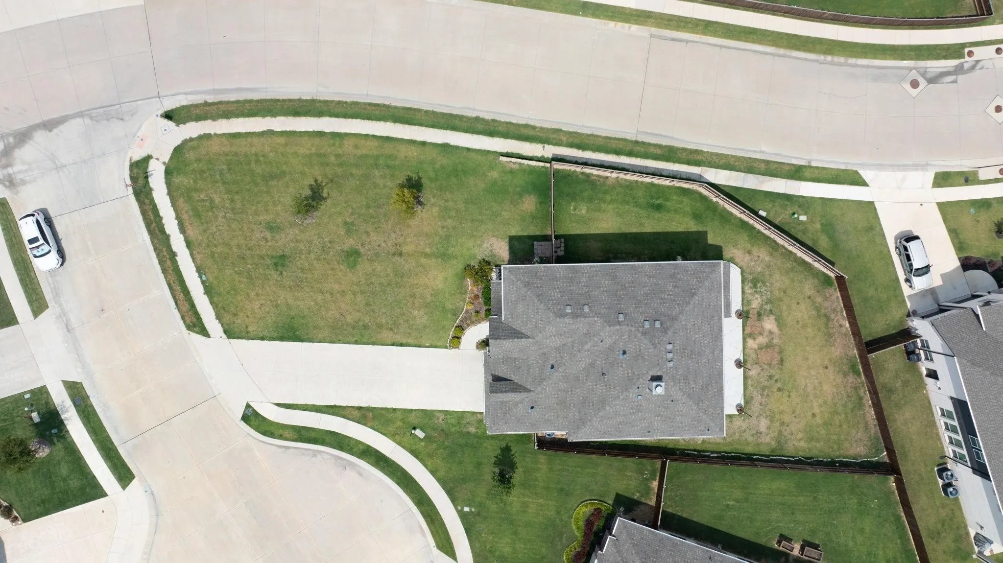 Aerial perspective showcasing the property's roofline, surrounding green lawns, perimeter fencing, and concrete driveways
