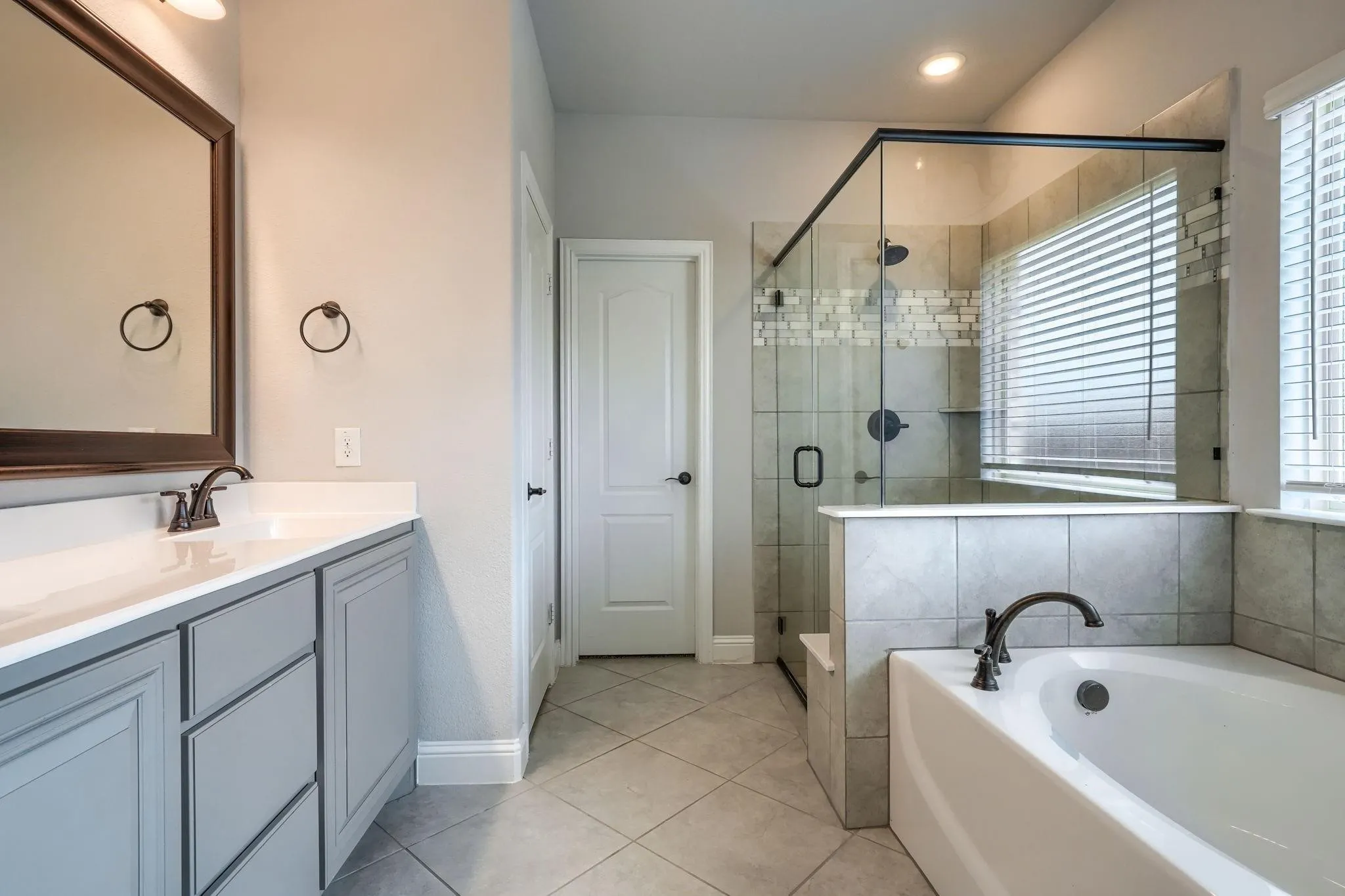 Spacious bathroom featuring a dual vanity with a white countertop, a walk-in shower with glass enclosure, a built-in bathtub, and diagonal tile flooring