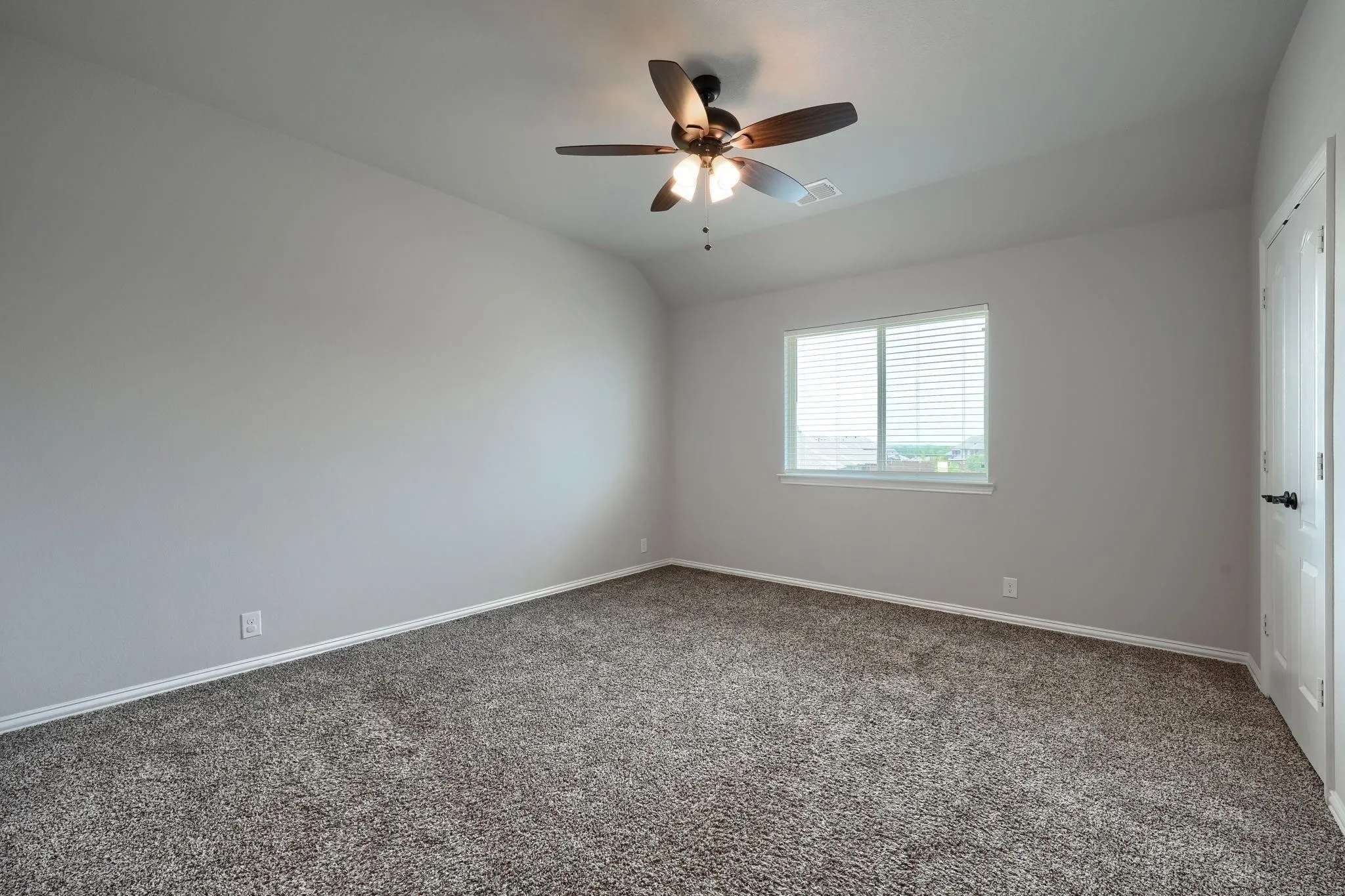 Neutral wall paint, brown carpet, ceiling fan with integrated lighting, white window blinds, and a white interior door with dark hardware