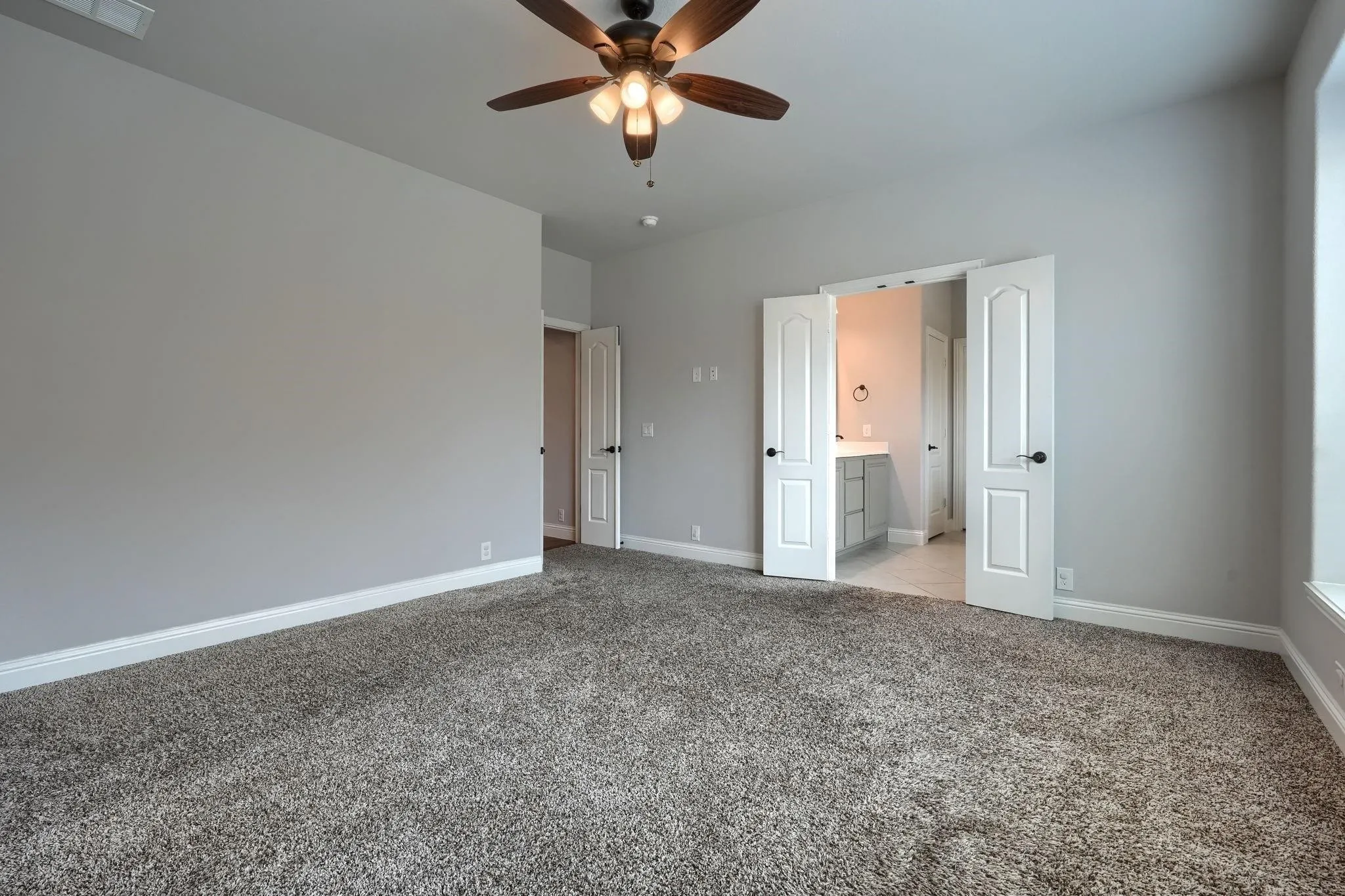Neutral gray wall color, textured carpeting, ceiling fan with integrated lighting, and white trim molding