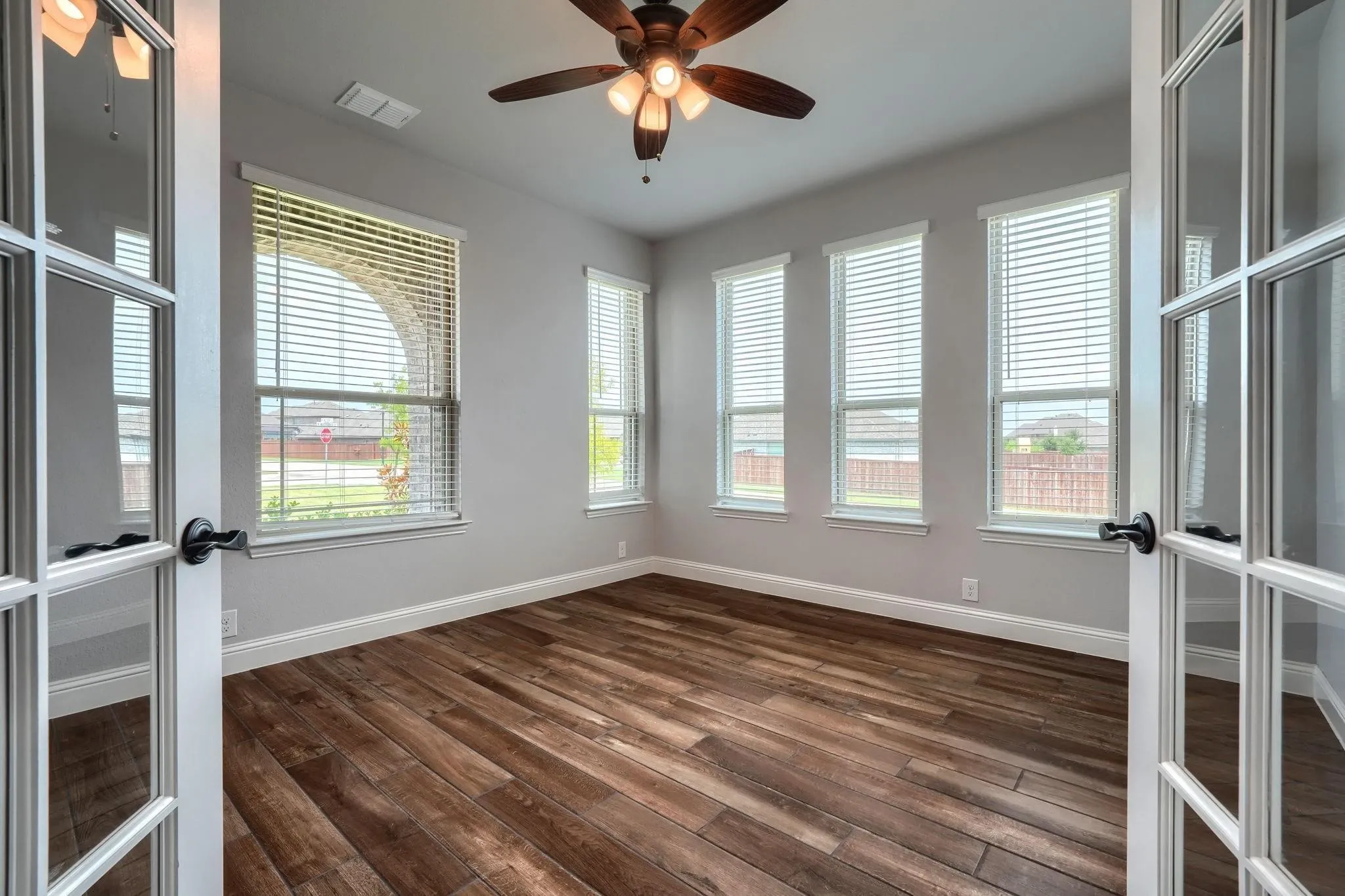 Wood-finish flooring, multiple windows with blinds, ceiling fan with integrated lighting, and white French doors