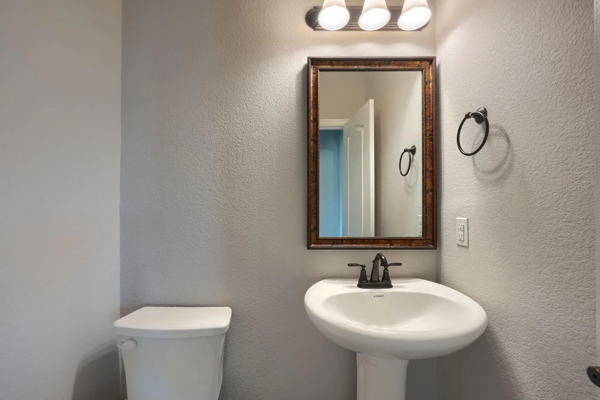 Pedestal sink with dark bronze faucet, framed mirror, and three-light vanity fixture