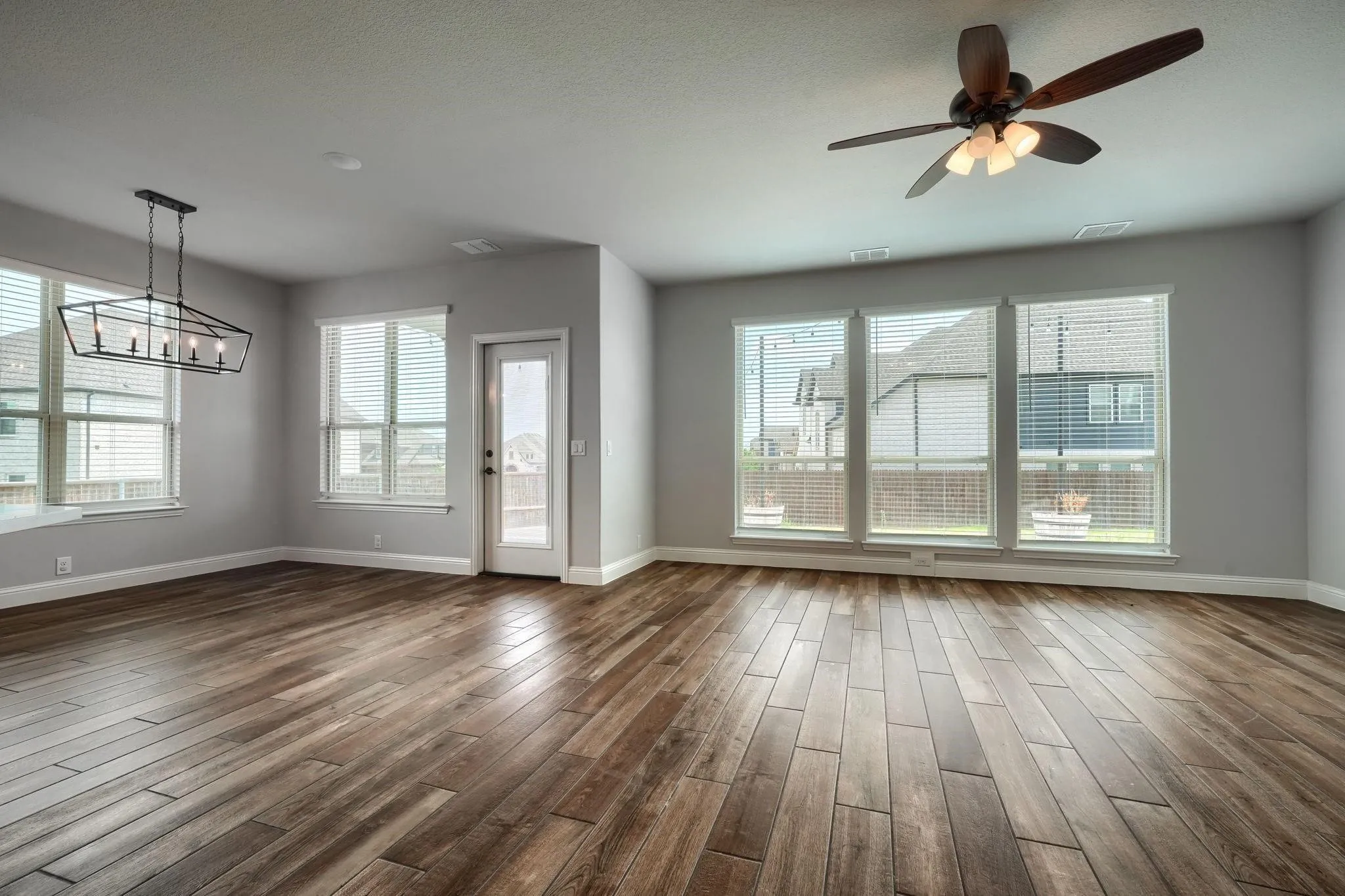 Spacious room featuring wood-finish flooring, multiple large windows, a built-in ceiling fan, and a contemporary linear chandelier