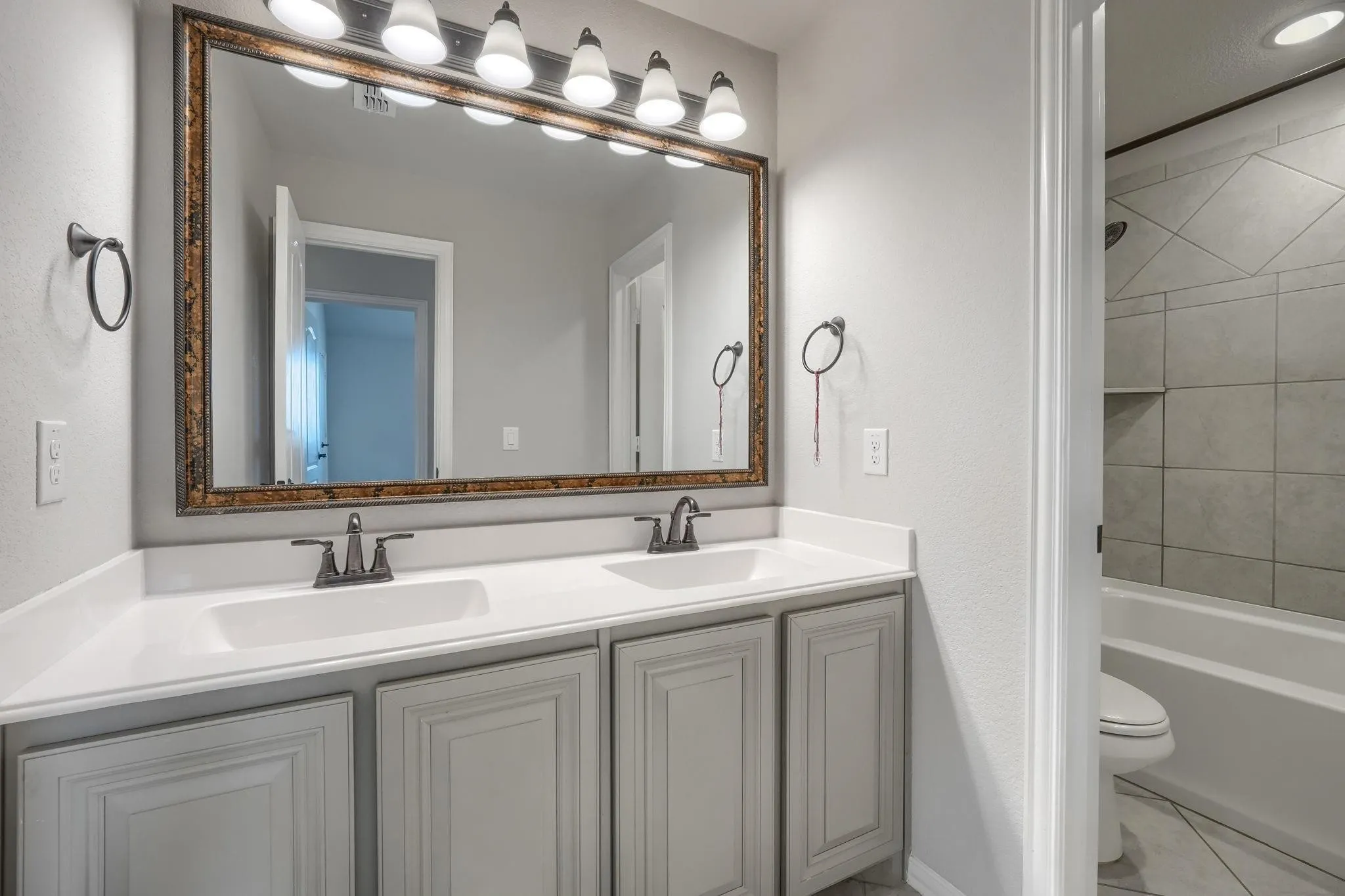 Dual vanity with integrated sinks, framed mirror, vanity lighting, and a tiled tub/shower combination with a built-in niche