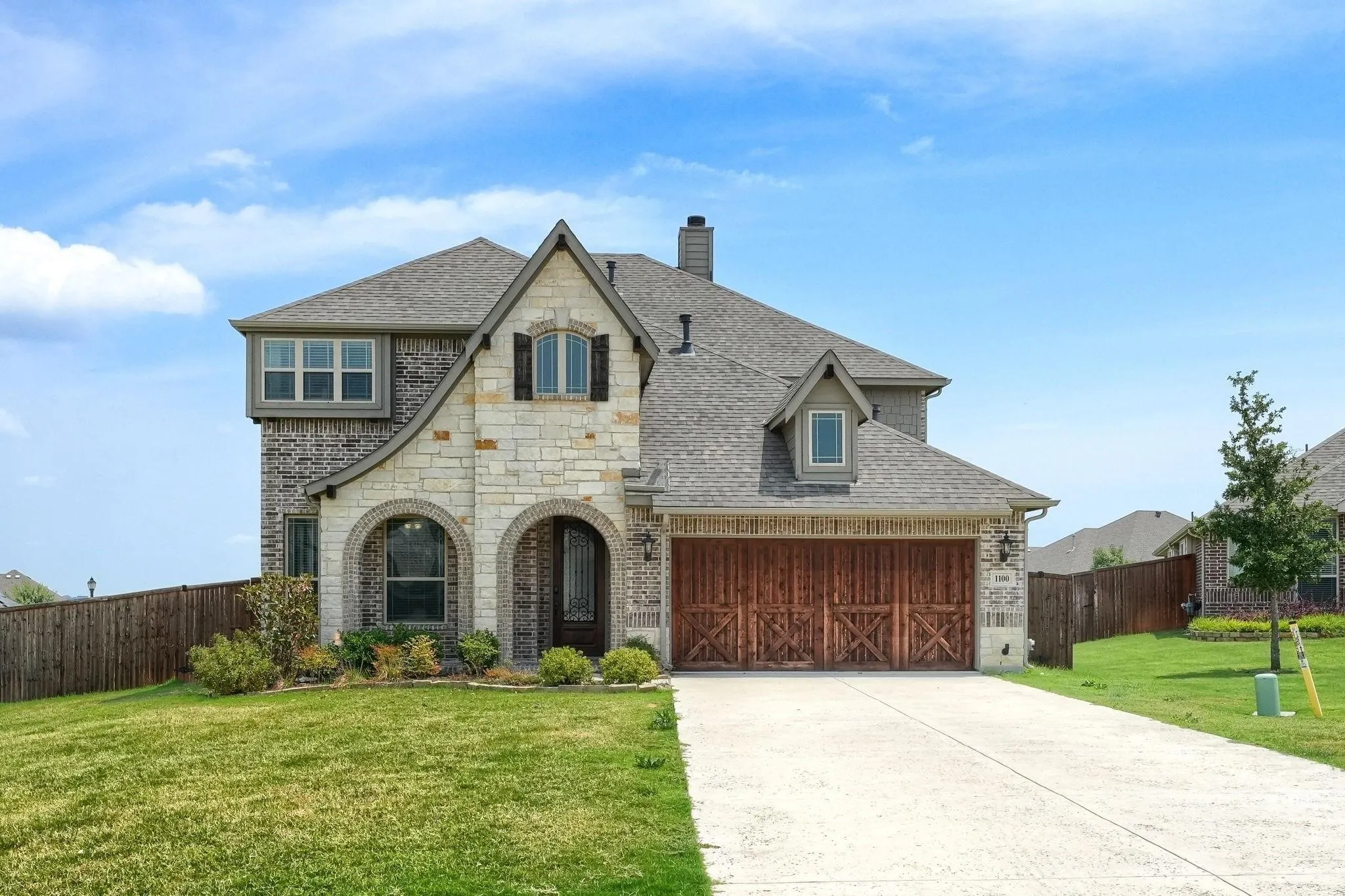 Stone and brick exterior with arched entryways, wood-finish garage doors, and a gabled roofline