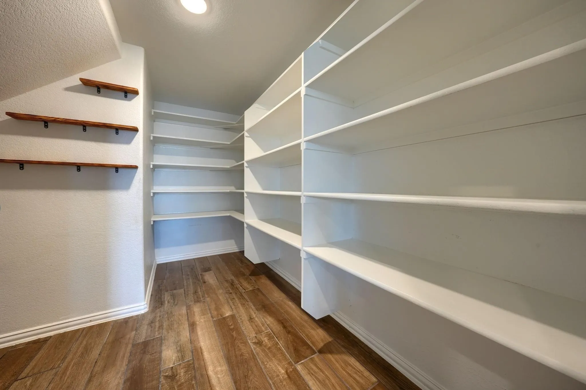 Extensive built-in shelving, additional wall-mounted wood shelves, wood-finish flooring, and recessed lighting