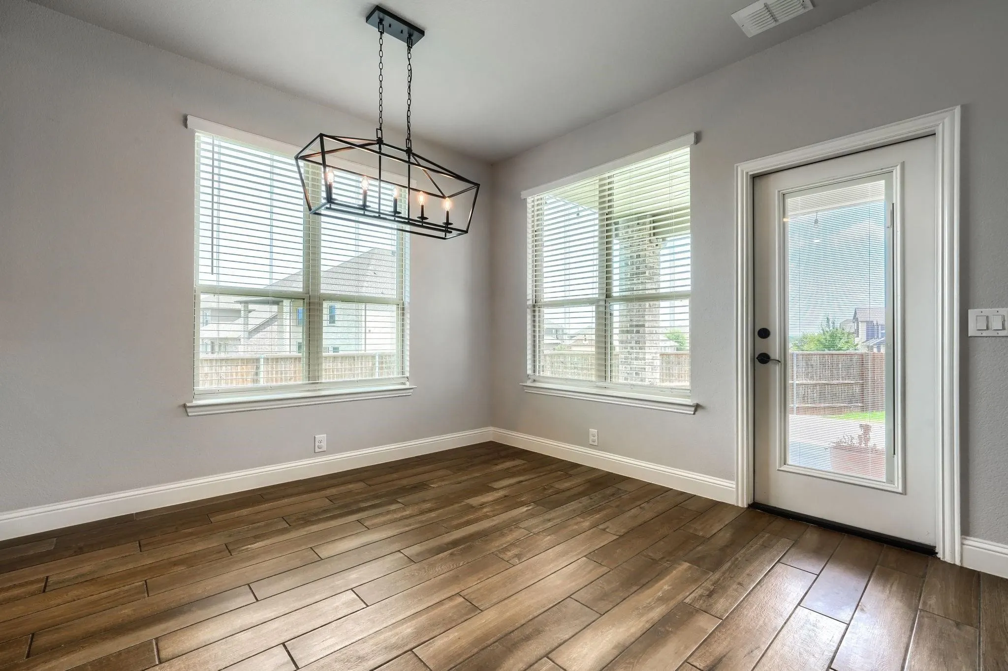 Wood-look tile flooring, two large windows with blinds, a modern black geometric chandelier, and a white door with a glass insert