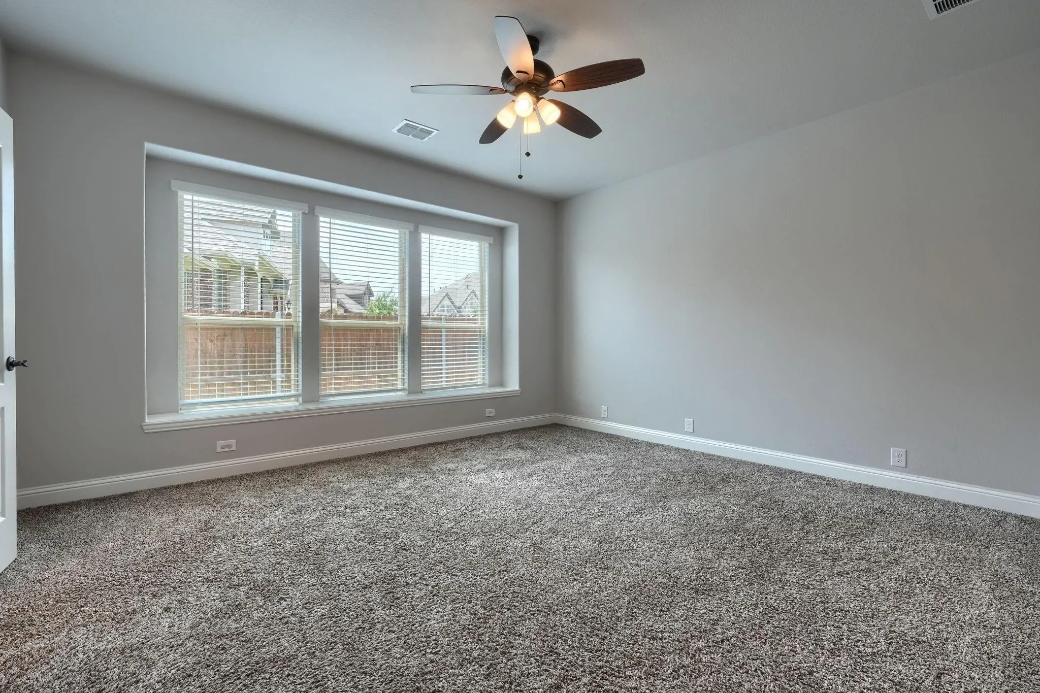 Recessed wall with three windows, a ceiling fan with integrated lighting, and neutral-toned wall-to-wall carpeting