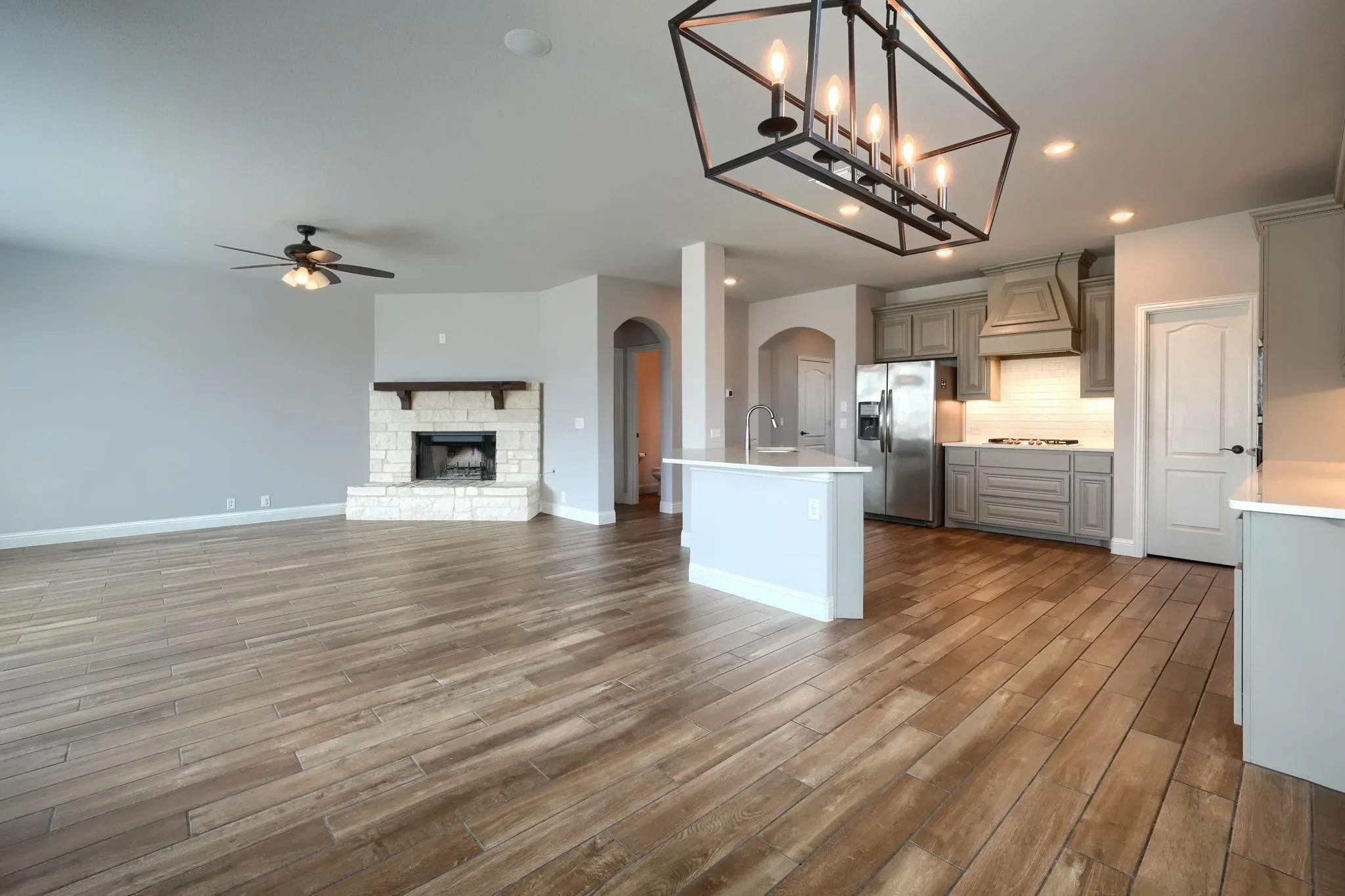 Spacious open-concept layout with wood-finish flooring, a stone fireplace, and an island kitchen featuring stainless steel appliances and a modern chandelier