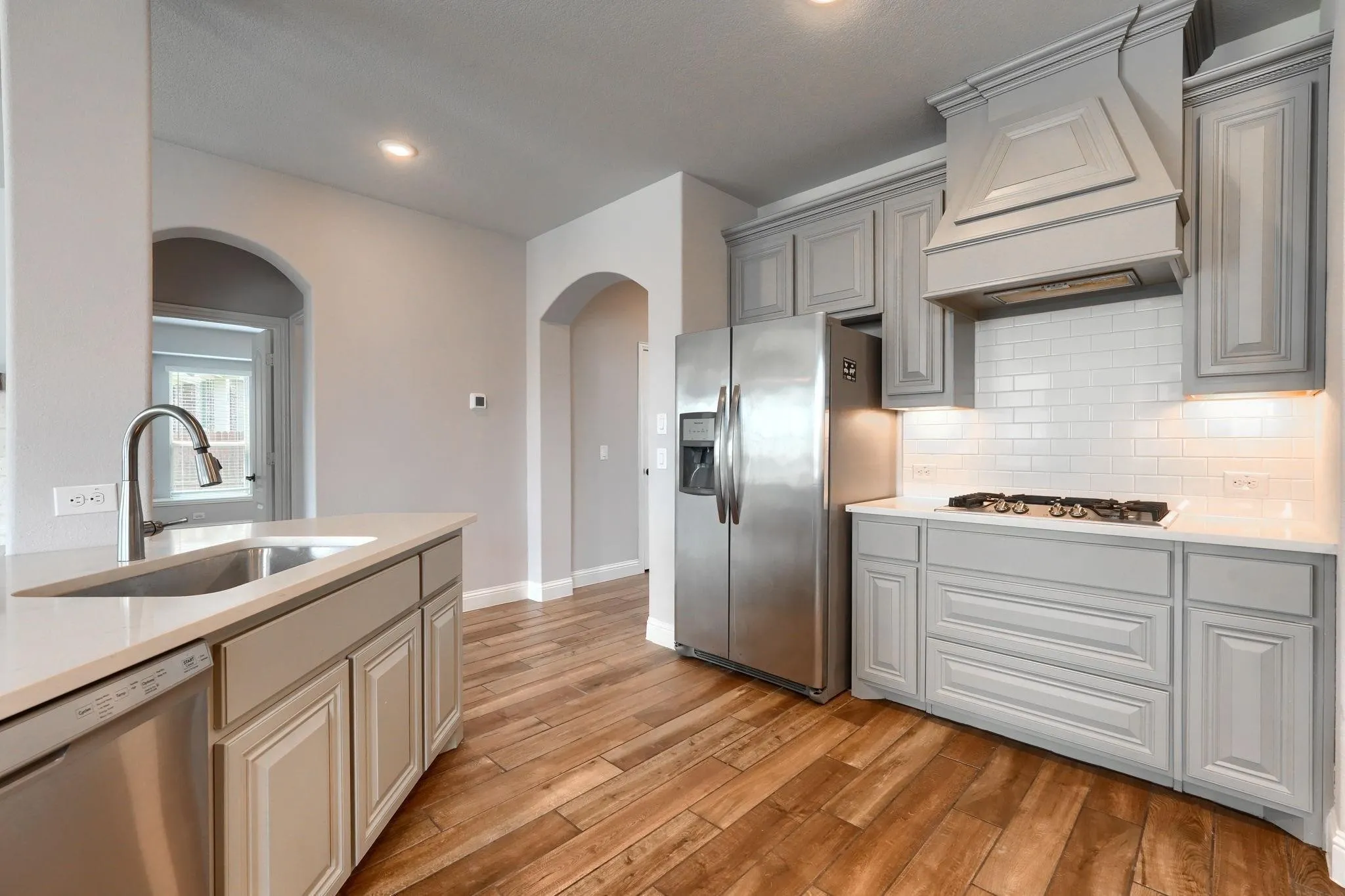 Stainless steel appliances, wood-finish flooring, light cabinetry, a kitchen island with an undermount sink, and recessed lighting