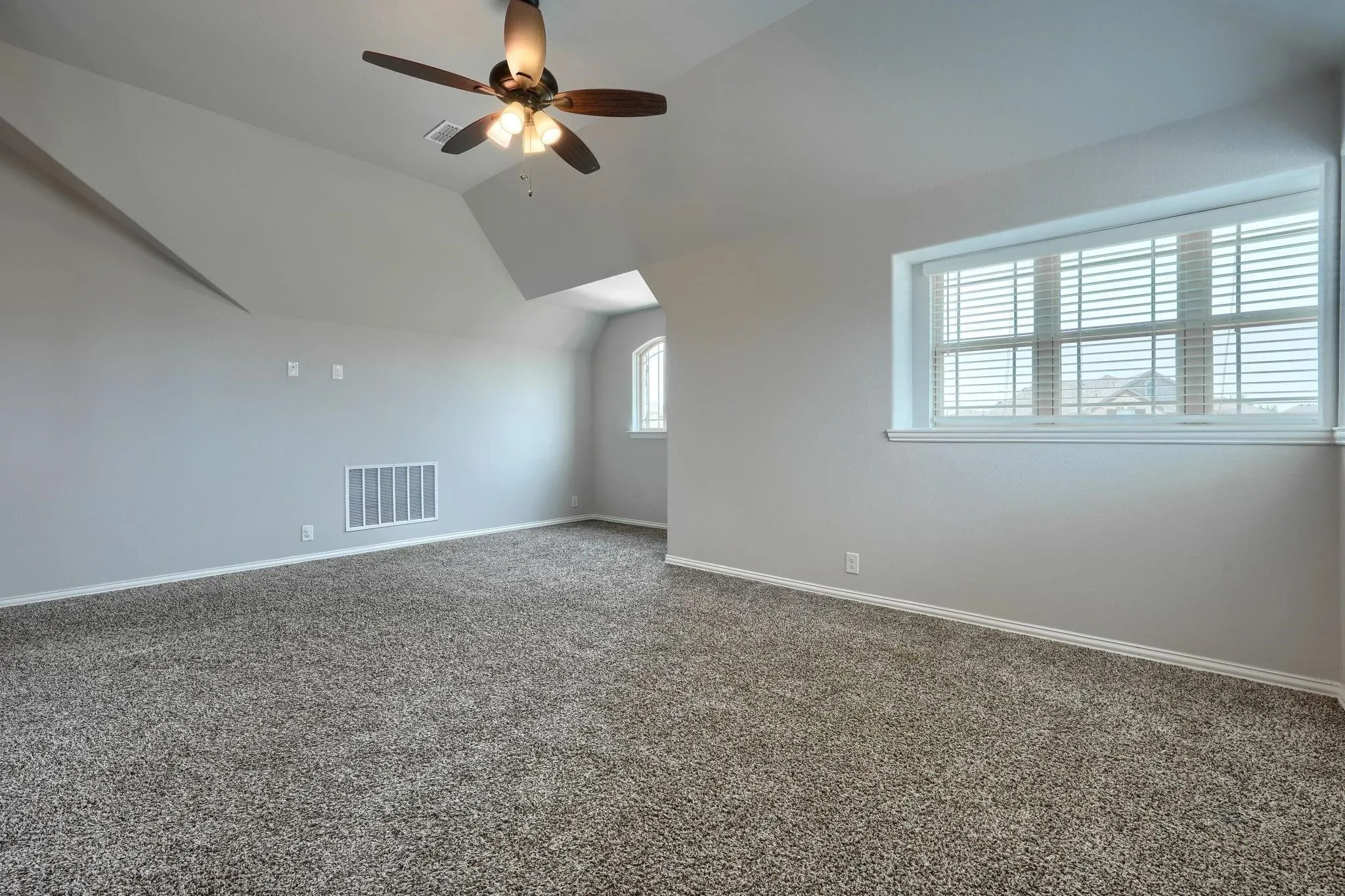 Spacious room featuring sloped ceilings, a ceiling fan with integrated lighting, and carpeted flooring