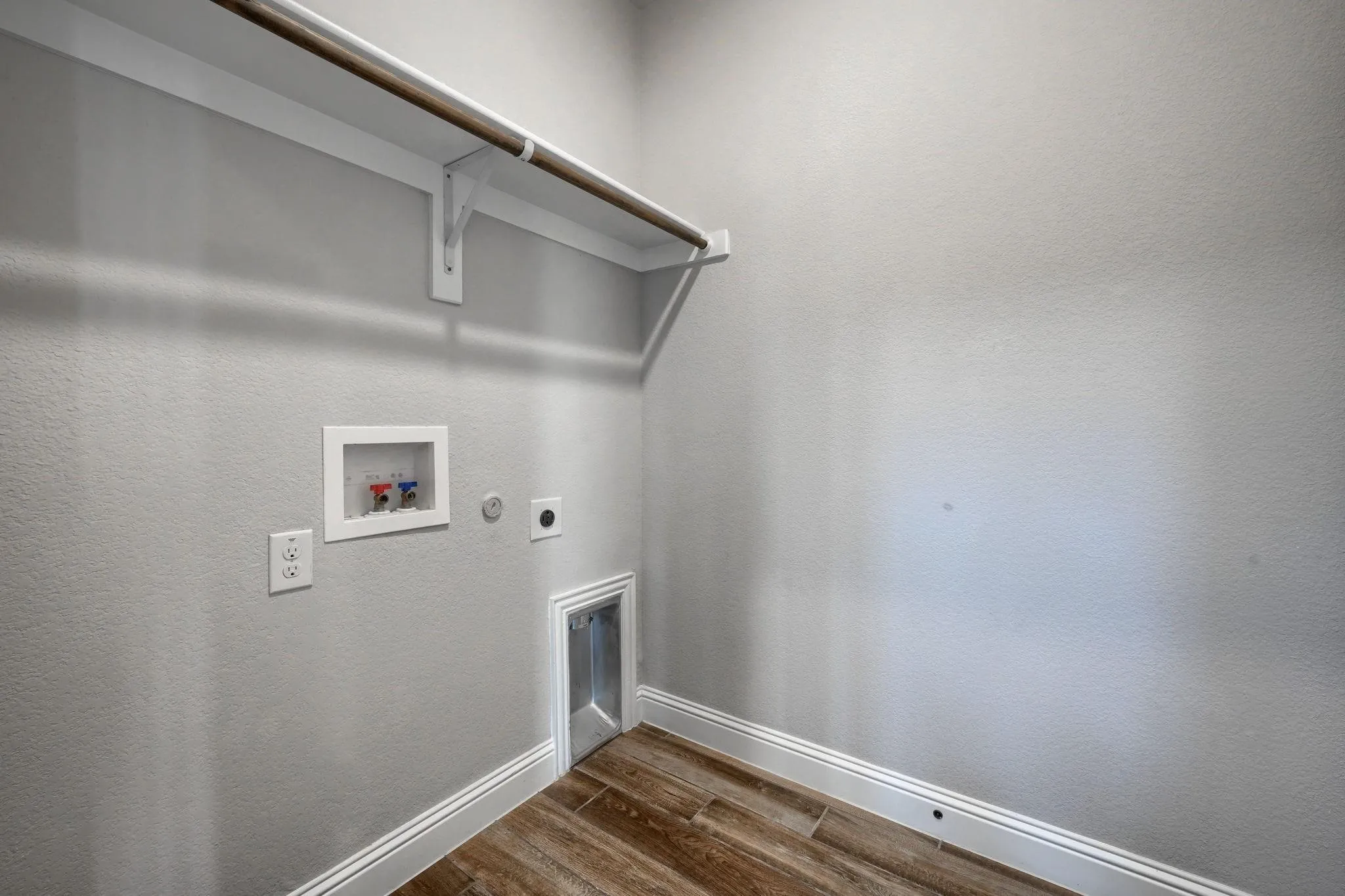 Laundry area with wood-finish flooring, white baseboards, a wall-mounted shelf, and a clothing rod