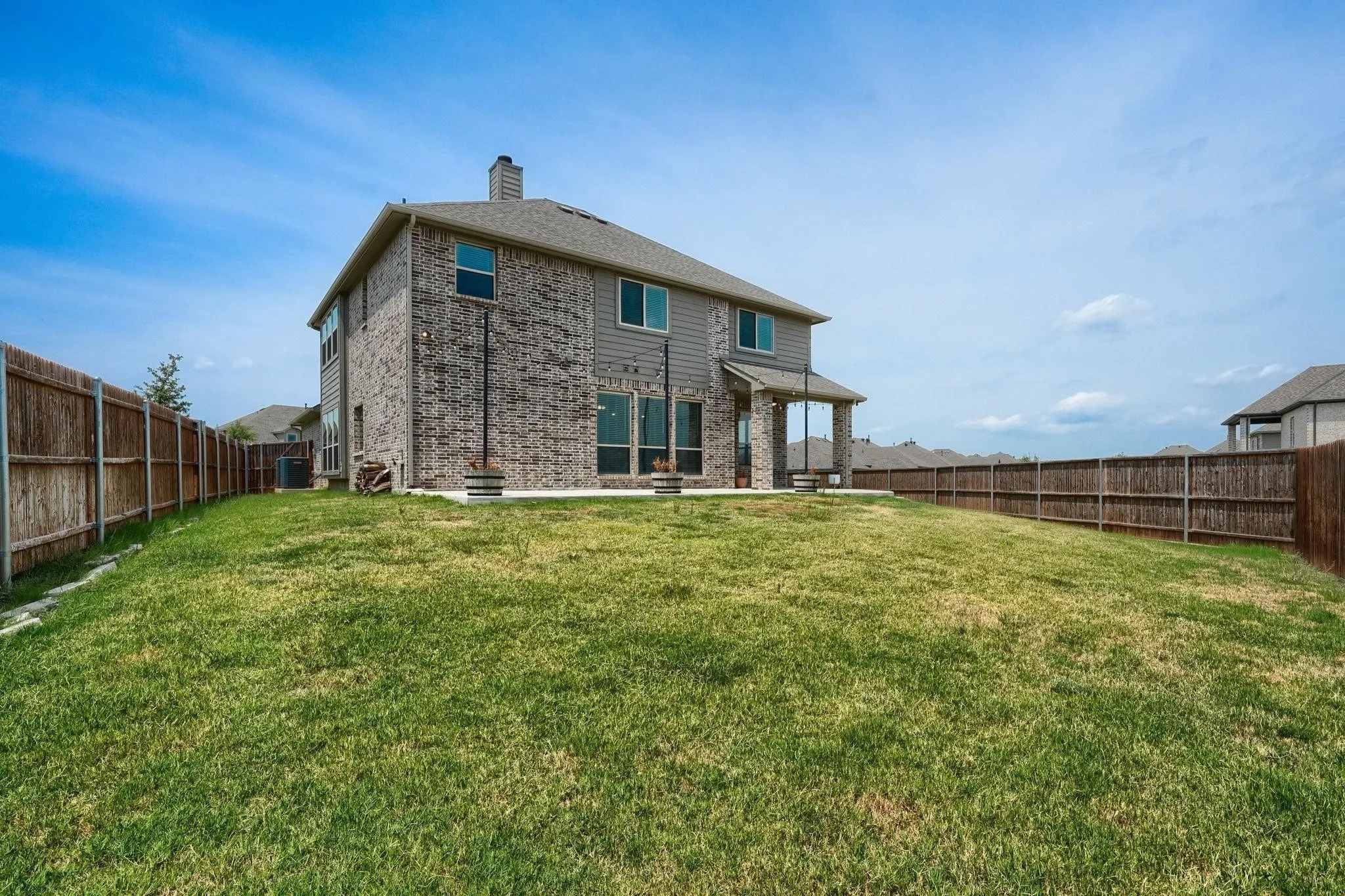 Expansive backyard featuring a manicured lawn, full perimeter fencing, and a covered patio