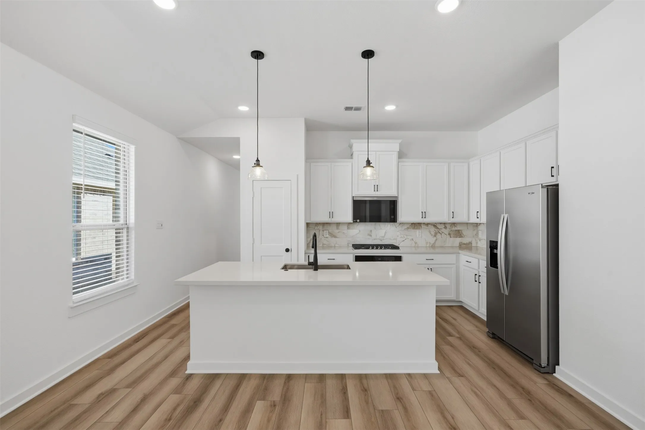 Kitchen featuring a large central island, pendant lighting, stainless steel appliances, white cabinetry, and wood-finish flooring